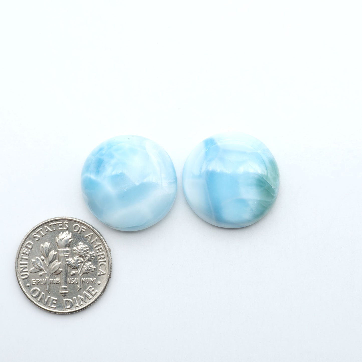 Larimar stone cabochons, cut and polished, blue and white gemstones on a white background, with a US dime for scale