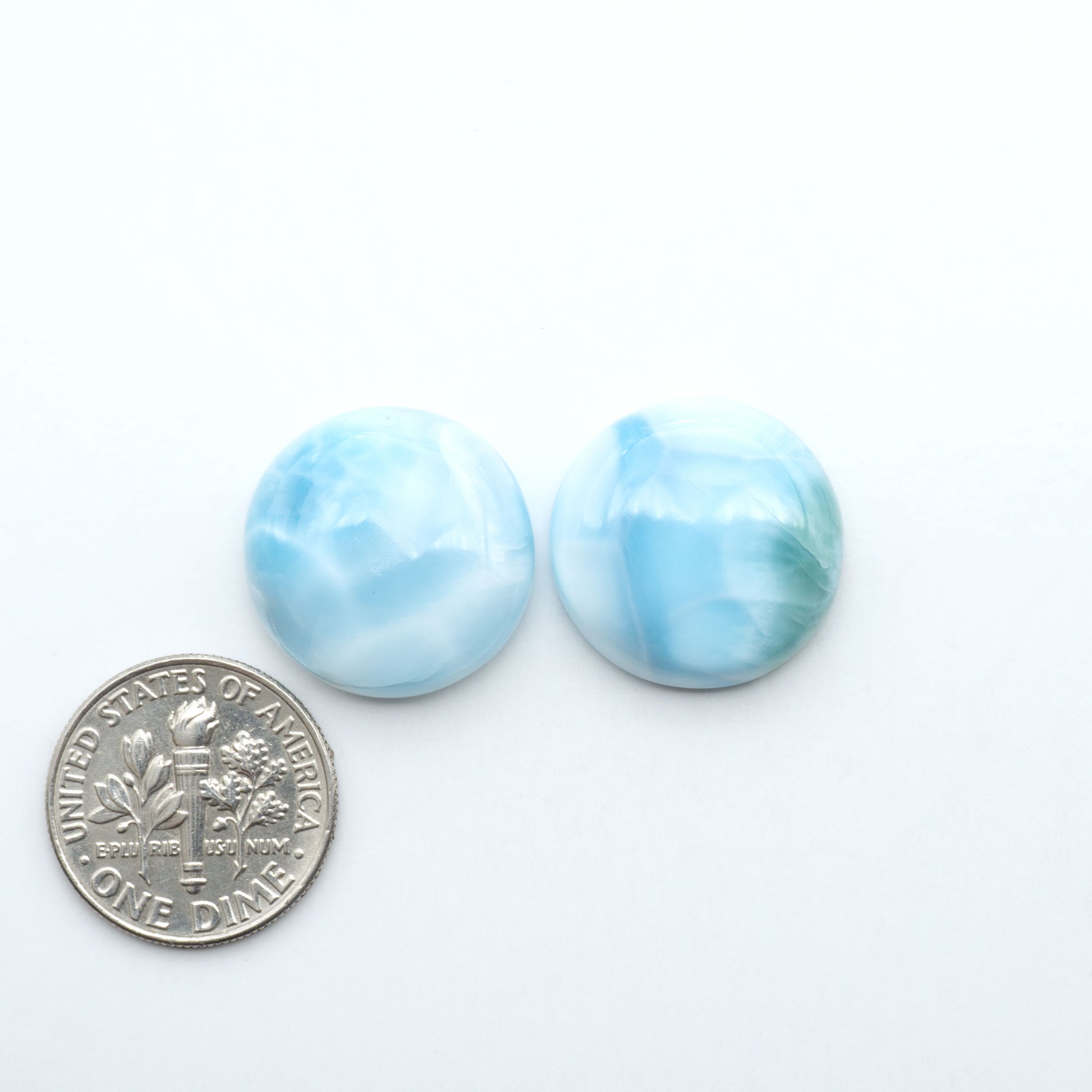 Larimar stone cabochons, cut and polished, blue and white gemstones on a white background, with a US dime for scale