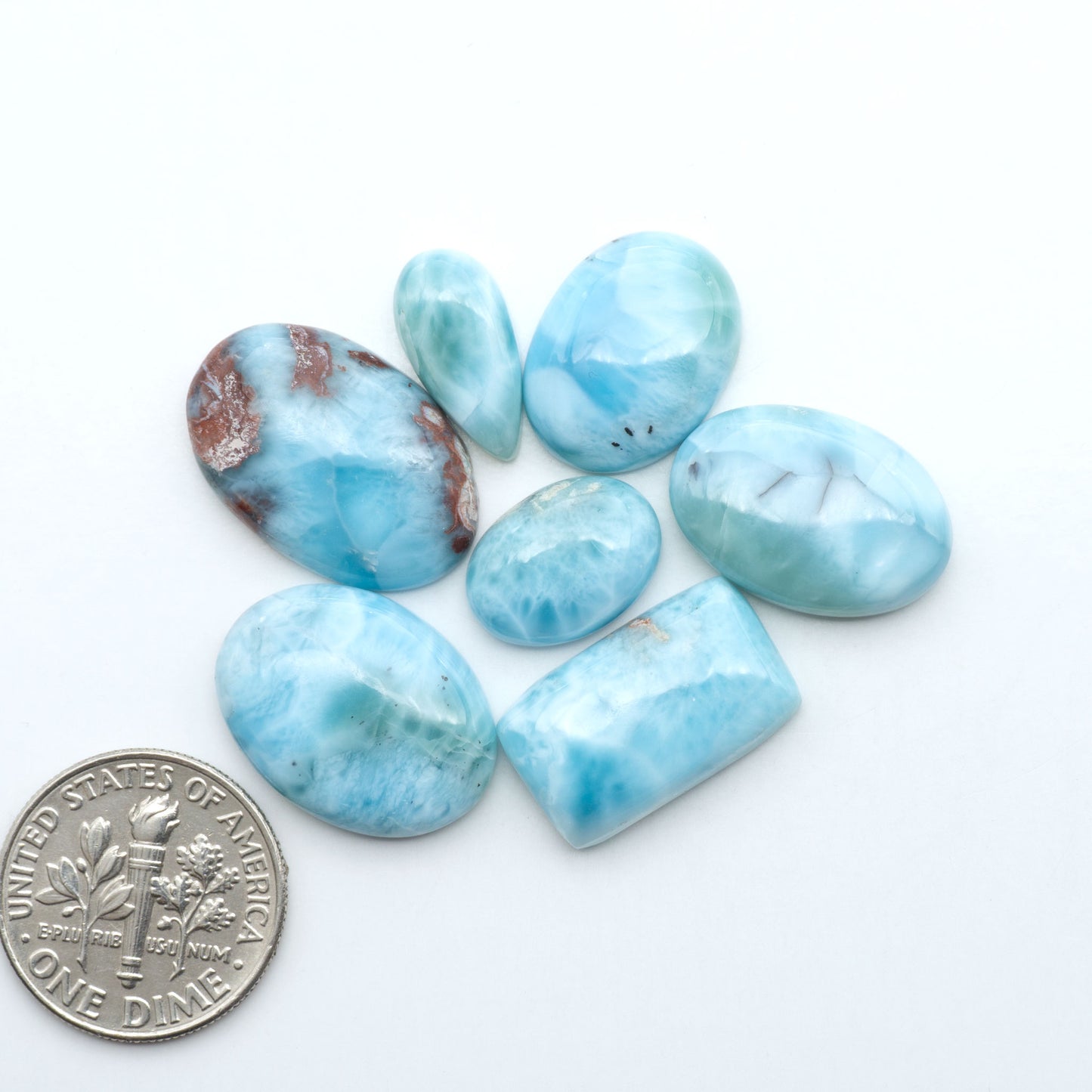 Larimar stone cabochons, cut and polished, blue and white gemstones on a white background, with a US dime for scale