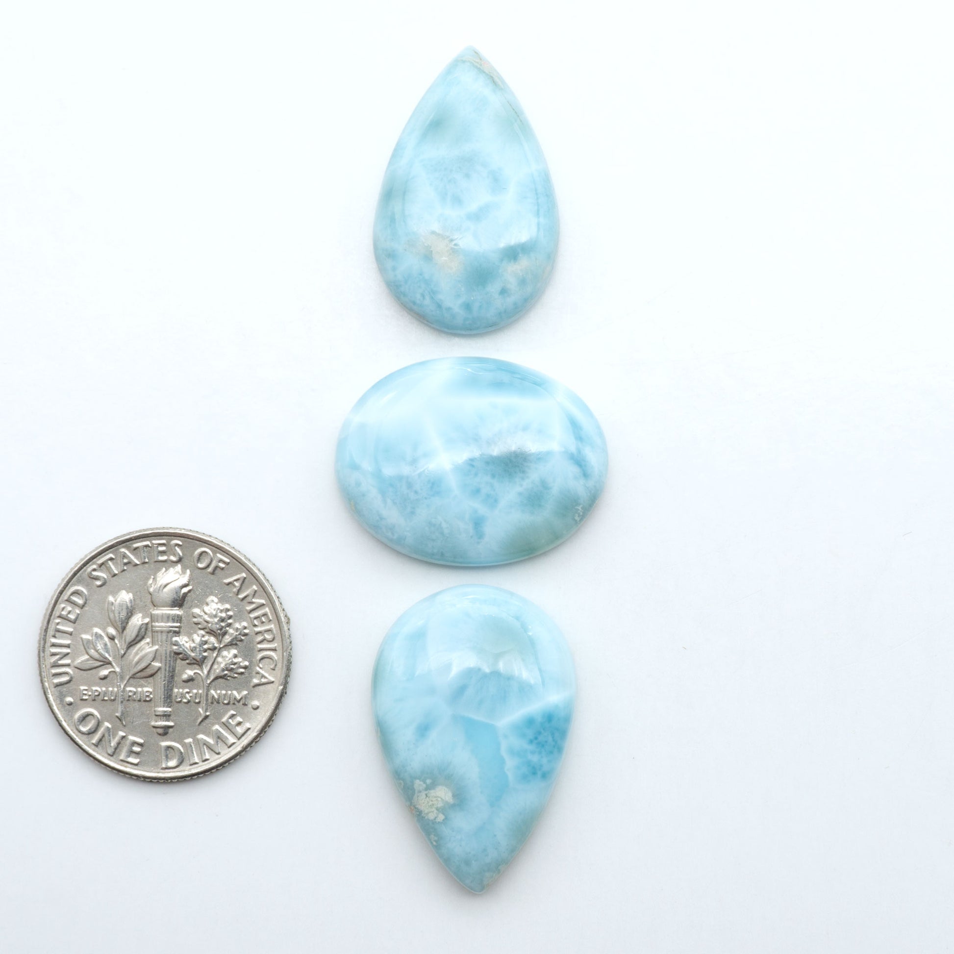 Larimar stone cabochons, cut and polished, blue and white gemstones on a white background, with a US dime for scale