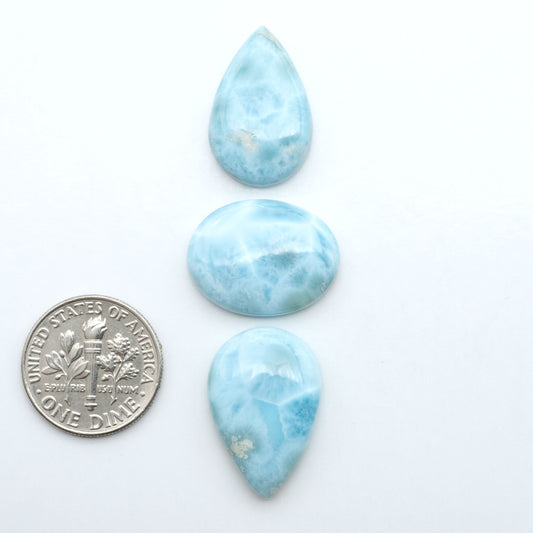 Larimar stone cabochons, cut and polished, blue and white gemstones on a white background, with a US dime for scale