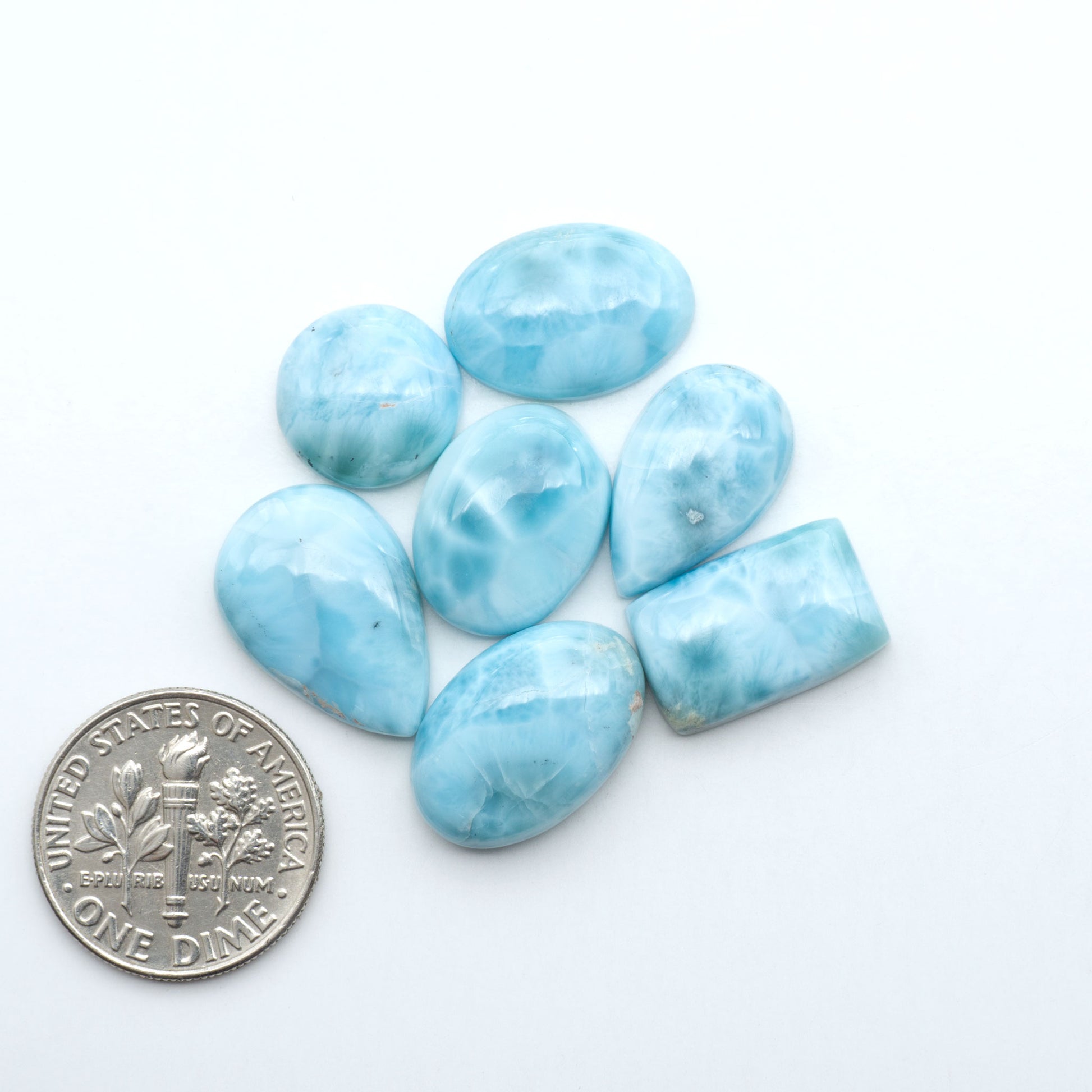 Larimar stone cabochons, cut and polished, blue and white gemstones on a white background, with a US dime for scale