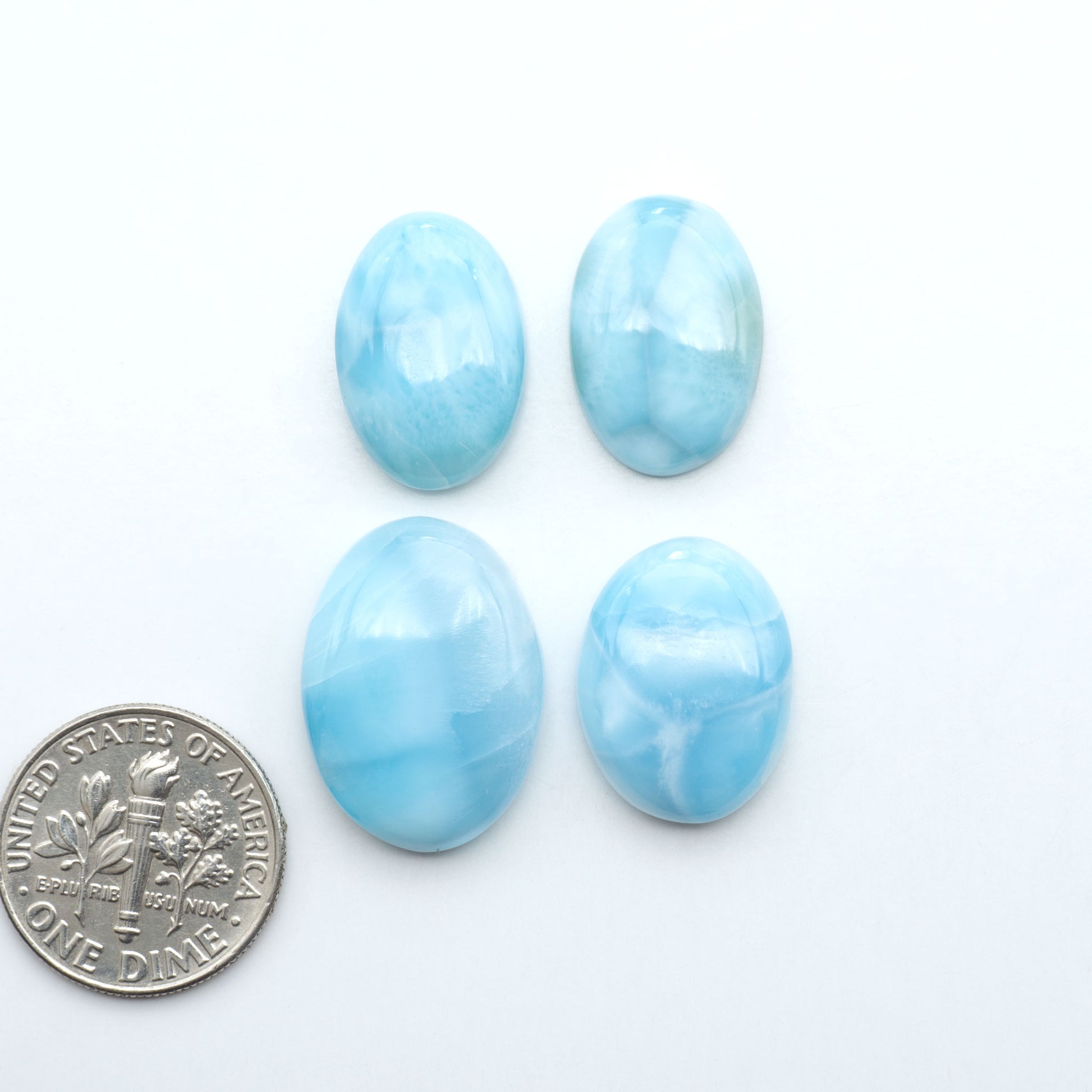 Larimar stone cabochons, cut and polished, blue and white gemstones on a white background, with a US dime for scale