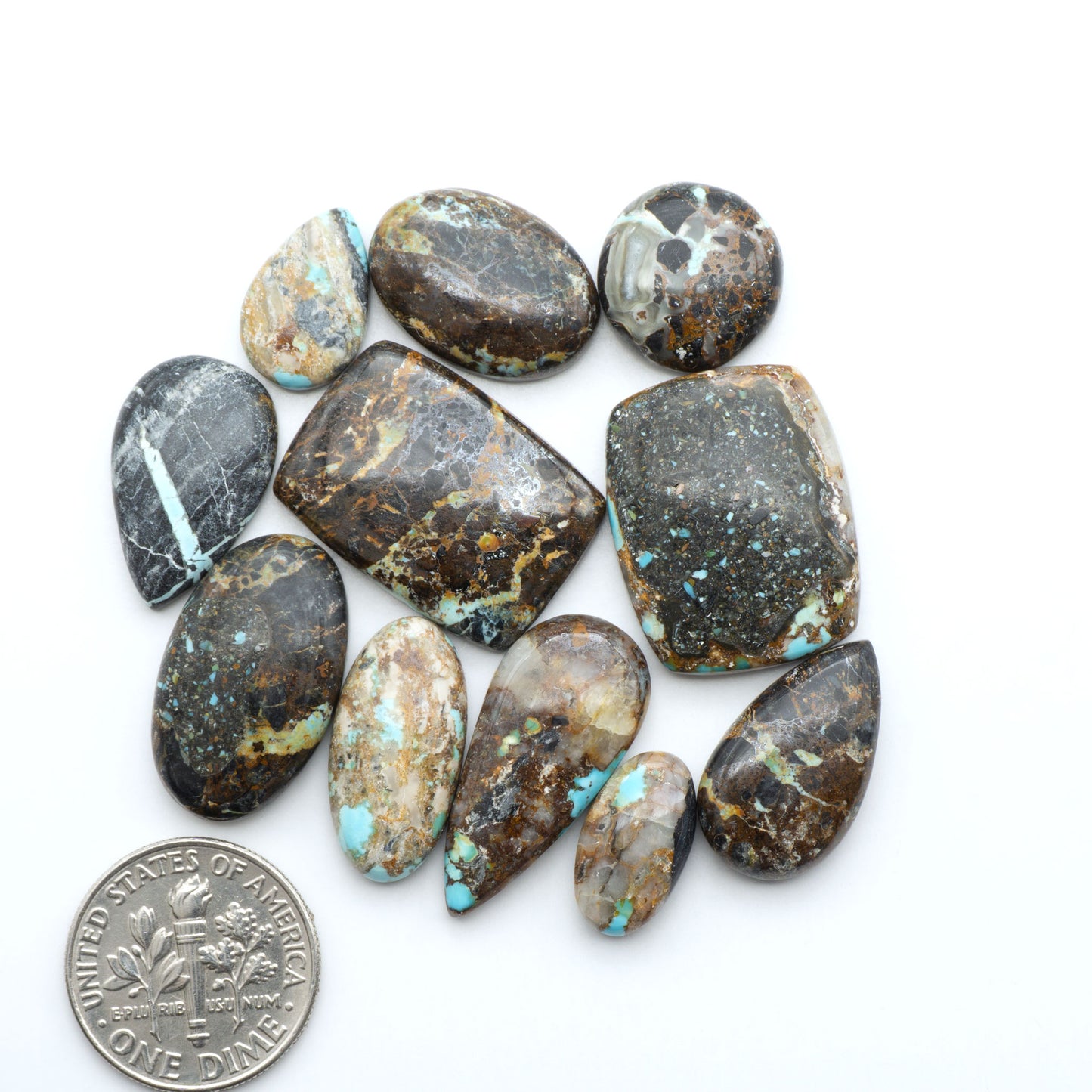 Black Jack turquoise cabochons, blue-green color with black matrix, polished stones on a white background with a US dime for scale