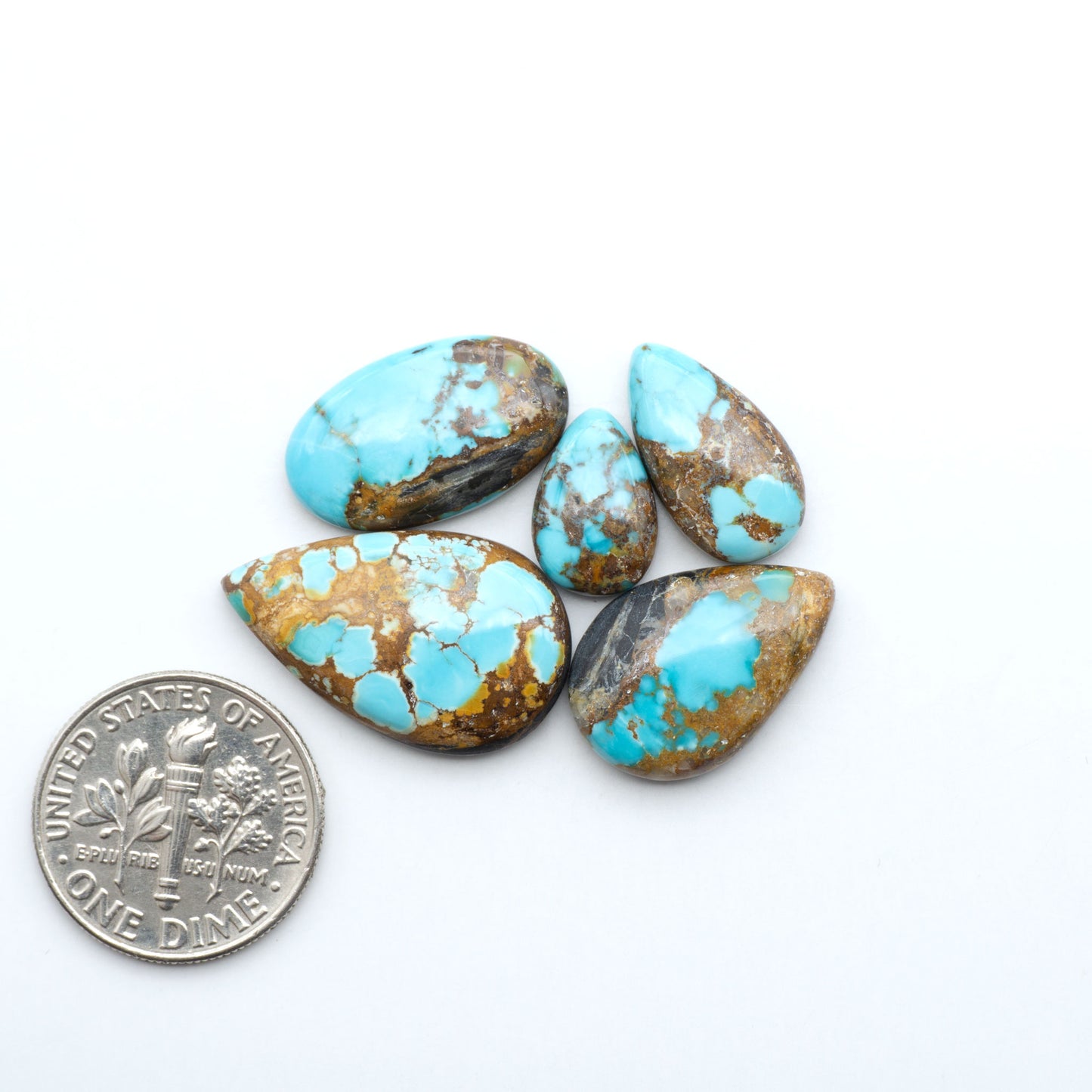 Black Jack turquoise cabochons, blue-green color with black matrix, polished stones on a white background with a US dime for scale