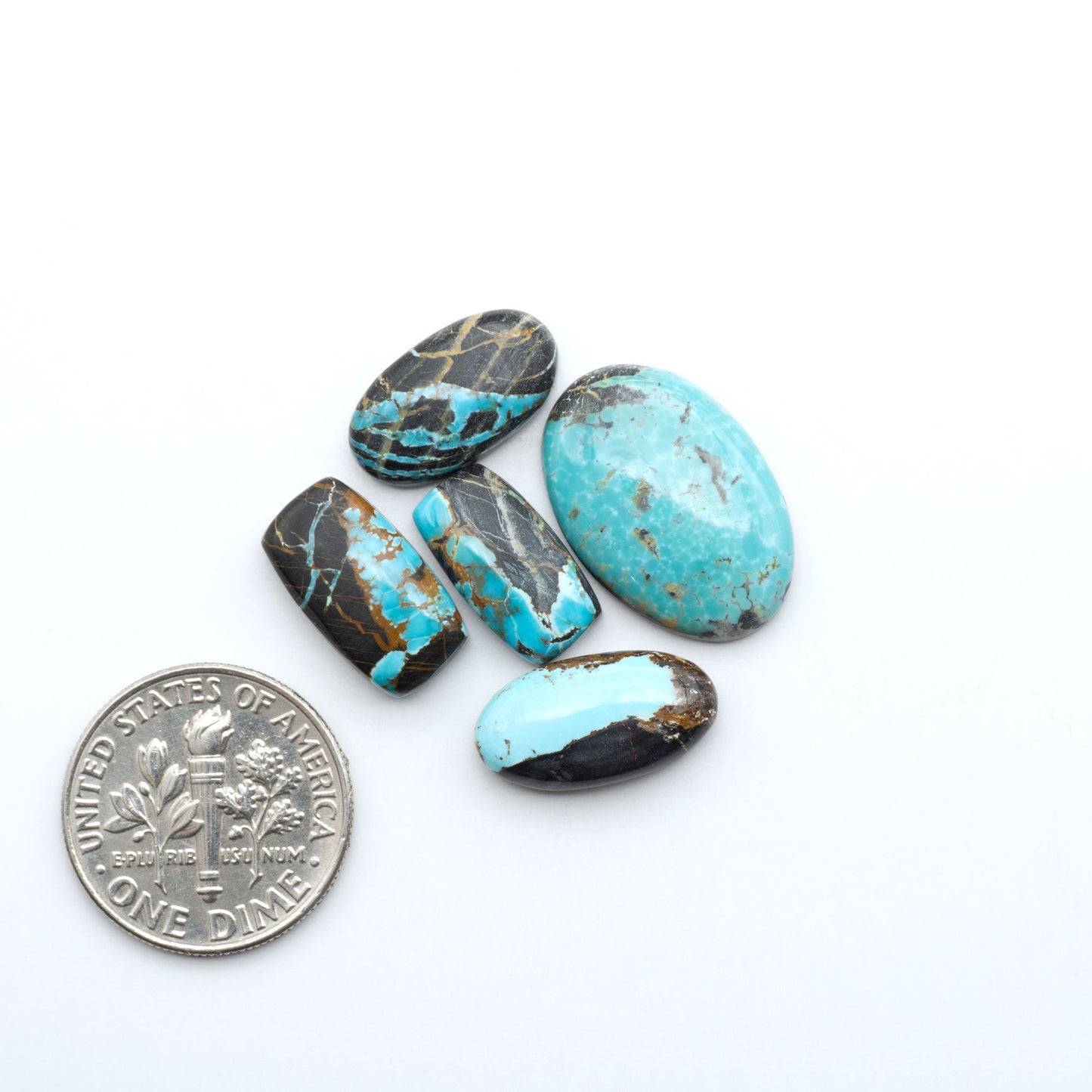 Black Jack turquoise cabochons, blue-green color with black matrix, polished stones on a white background with a US dime for scale