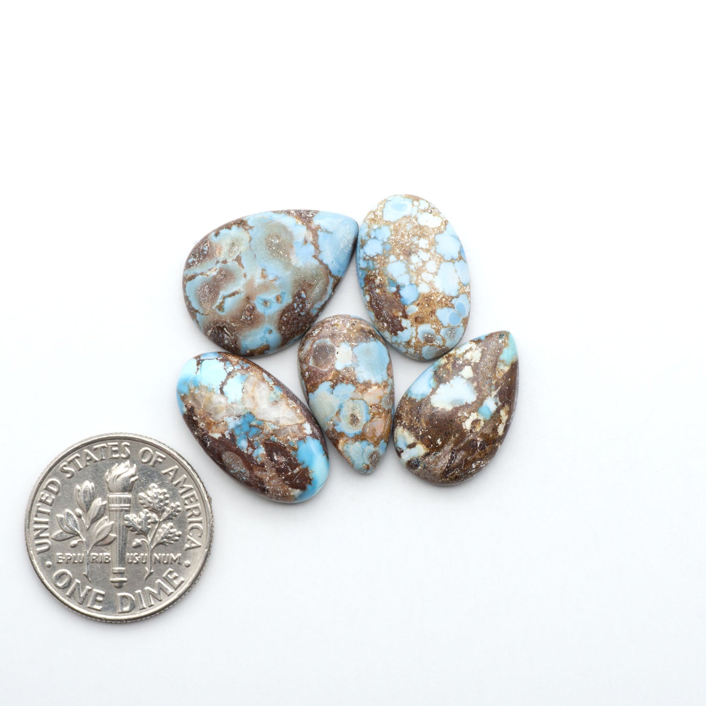 Golden Hills Turquoise cabochons, icy blue to lavender tones with chocolate matrix, polished stones on a white background with a US dime for scale