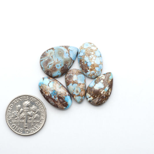 Golden Hills Turquoise cabochons, icy blue to lavender tones with chocolate matrix, polished stones on a white background with a US dime for scale