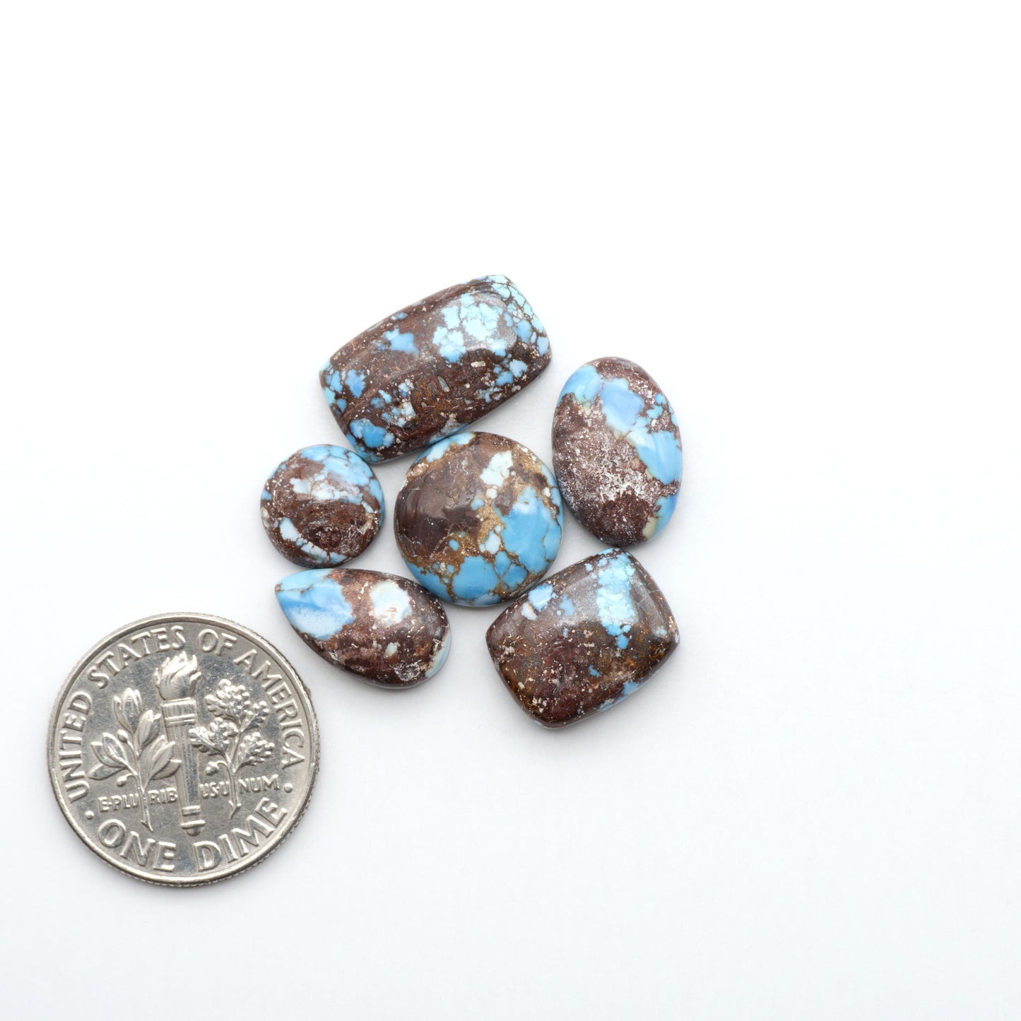 Golden Hills Turquoise cabochons, icy blue to lavender tones with chocolate matrix, polished stones on a white background with a US dime for scale