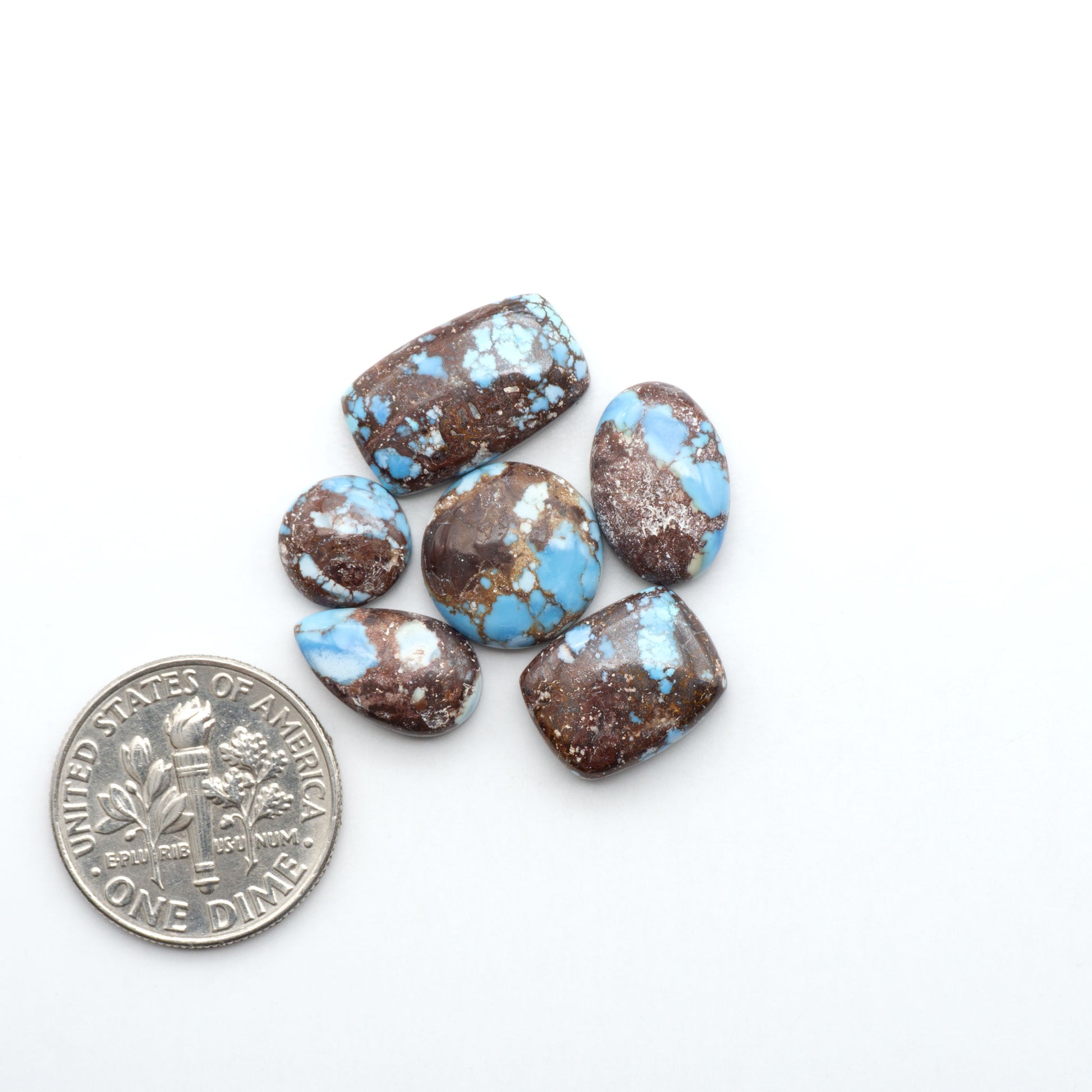 Golden Hills Turquoise cabochons, icy blue to lavender tones with chocolate matrix, polished stones on a white background with a US dime for scale