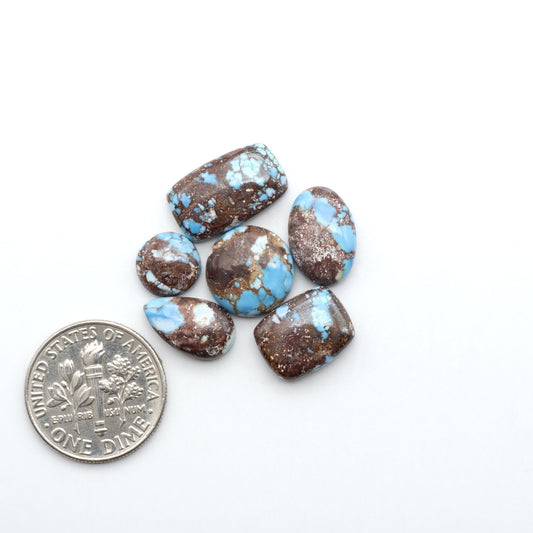 Golden Hills Turquoise cabochons, icy blue to lavender tones with chocolate matrix, polished stones on a white background with a US dime for scale