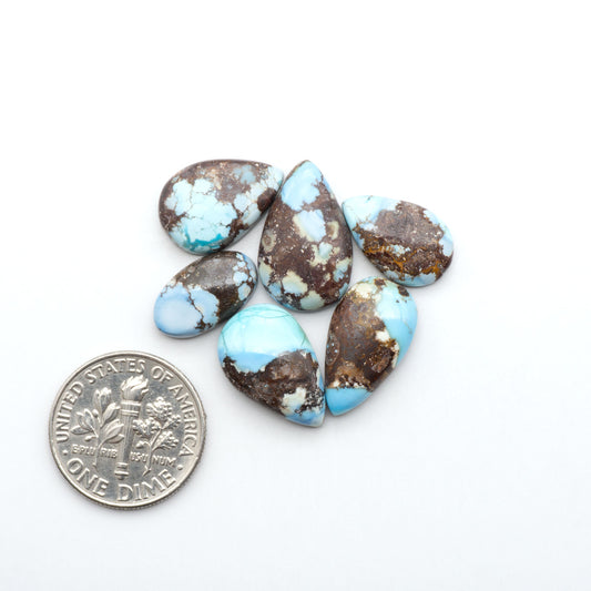 Golden Hills Turquoise cabochons, icy blue to lavender tones with chocolate matrix, polished stones on a white background with a US dime for scale