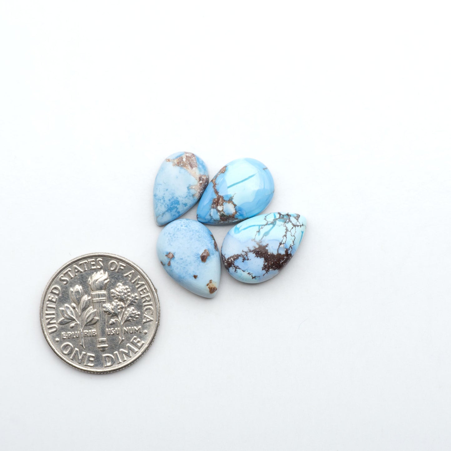 Golden Hills Turquoise cabochons, icy blue to lavender tones with chocolate matrix, polished stones on a white background with a US dime for scale