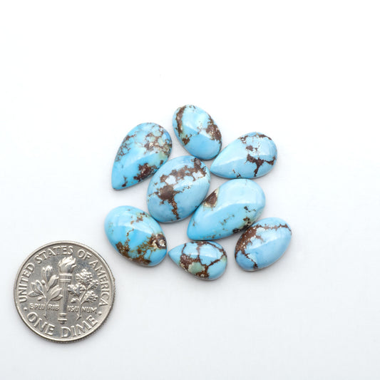 Golden Hills Turquoise cabochons, icy blue to lavender tones with chocolate matrix, polished stones on a white background with a US dime for scale