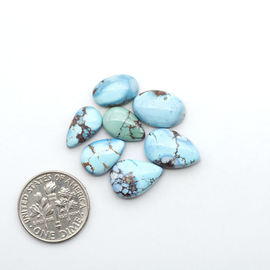Golden Hills Turquoise cabochons, icy blue to lavender tones with chocolate matrix, polished stones on a white background with a US dime for scale