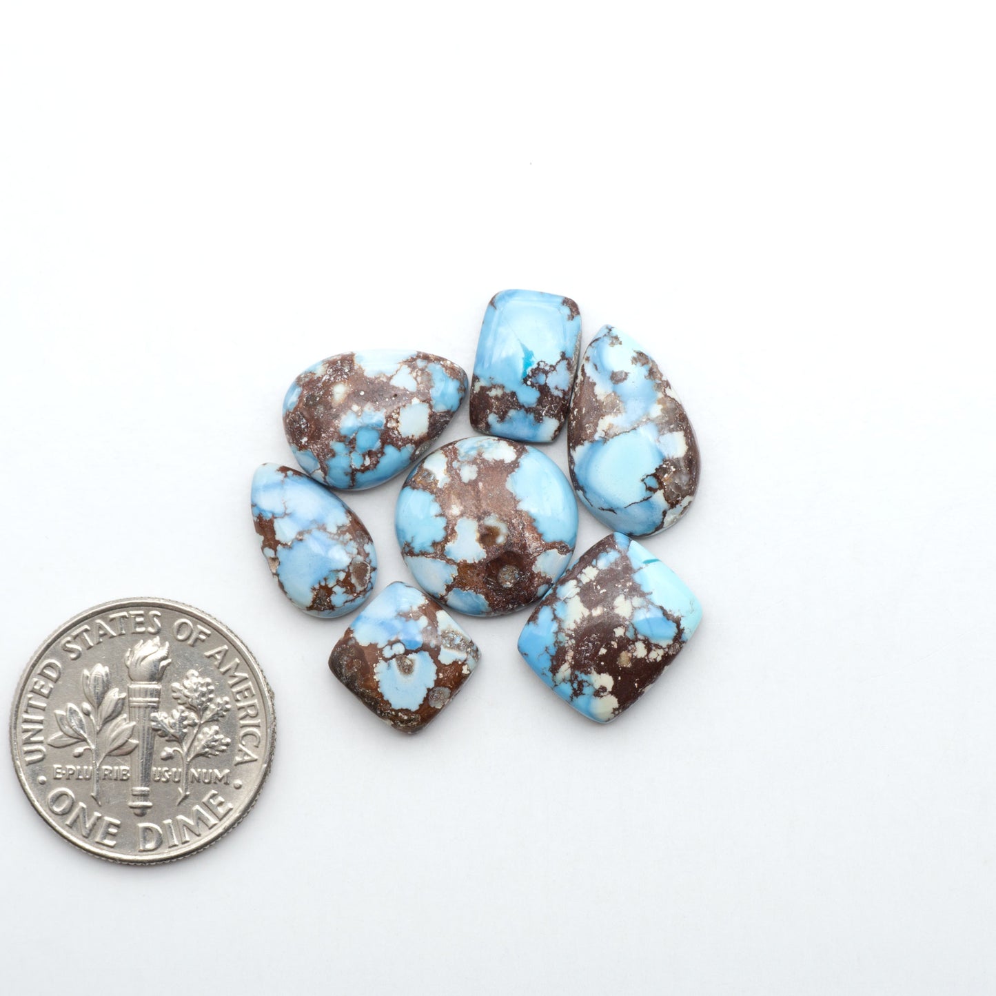 Golden Hills Turquoise cabochons, icy blue to lavender tones with chocolate matrix, polished stones on a white background with a US dime for scale