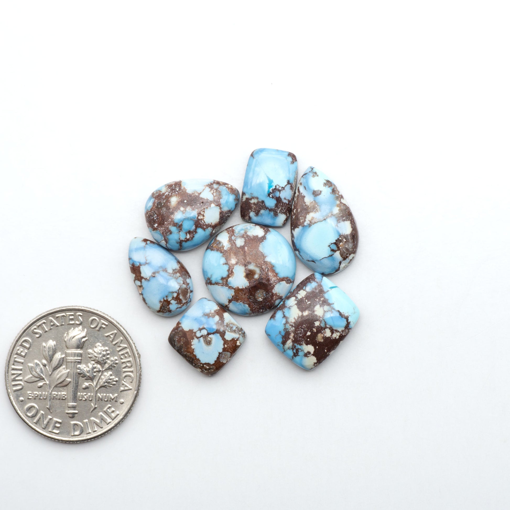 Golden Hills Turquoise cabochons, icy blue to lavender tones with chocolate matrix, polished stones on a white background with a US dime for scale