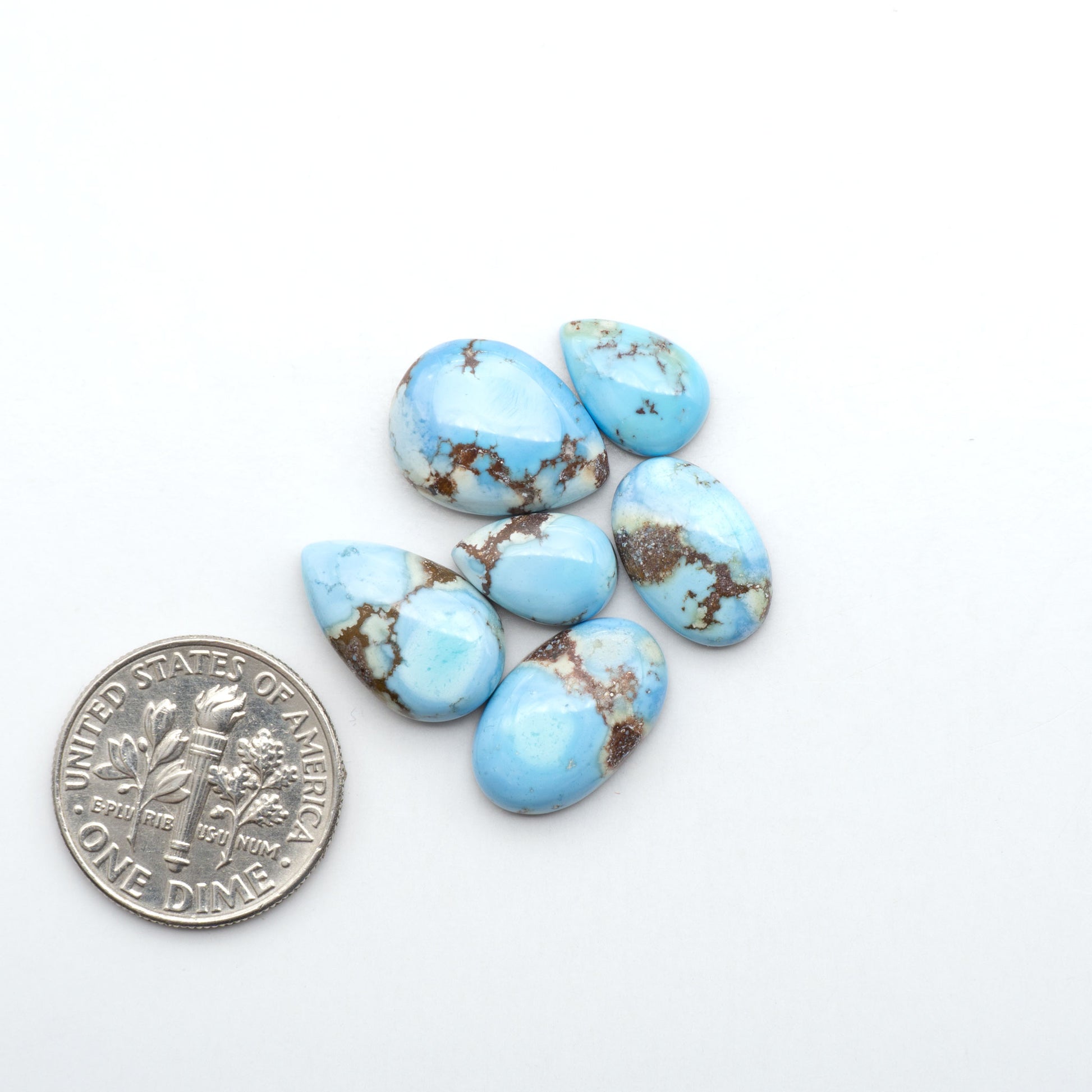 Golden Hills Turquoise cabochons, icy blue to lavender tones with chocolate matrix, polished stones on a white background with a US dime for scale