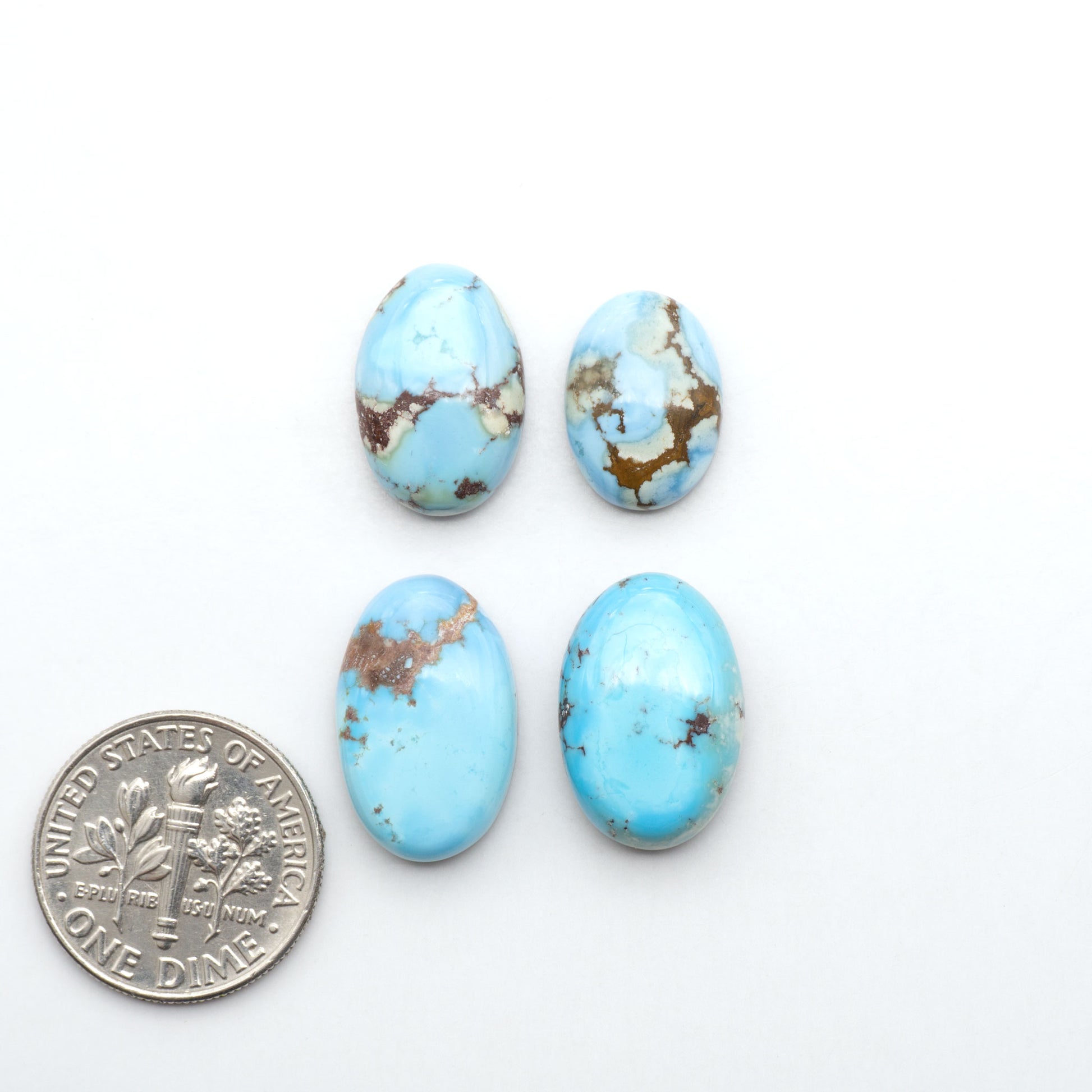 Golden Hills Turquoise cabochons, icy blue to lavender tones with chocolate matrix, polished stones on a white background with a US dime for scale