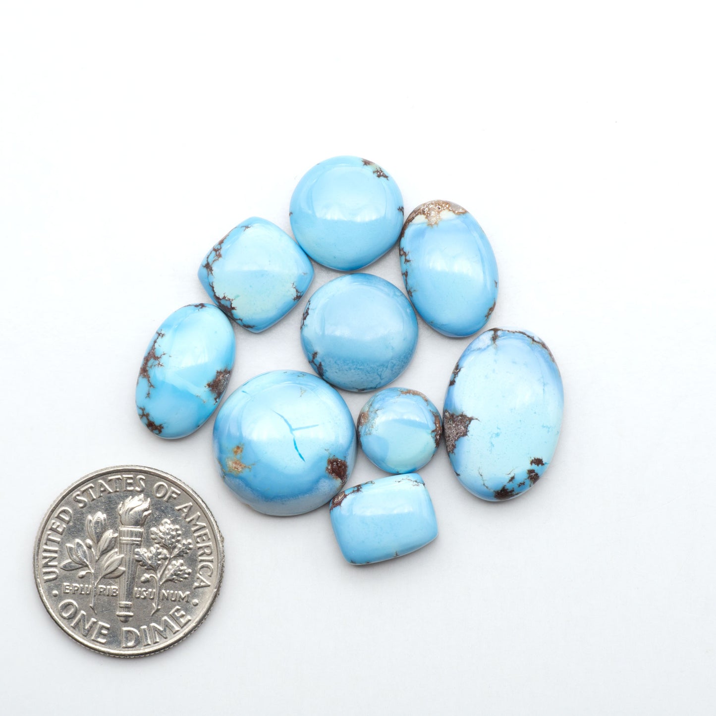 Golden Hills Turquoise cabochons, icy blue to lavender tones with chocolate matrix, polished stones on a white background with a US dime for scale