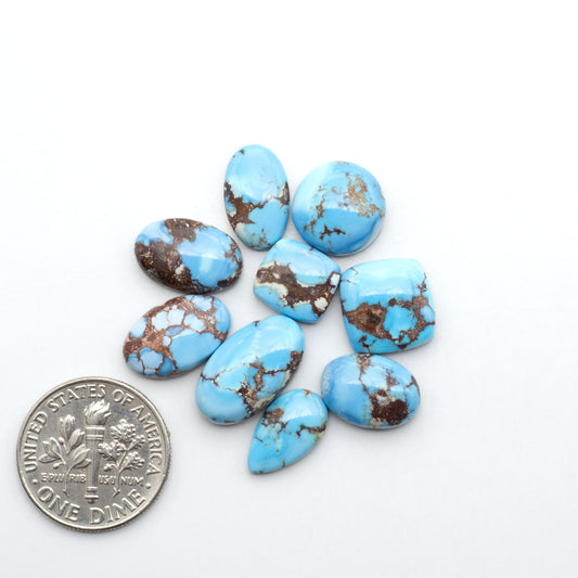 Golden Hills Turquoise cabochons, icy blue to lavender tones with chocolate matrix, polished stones on a white background with a US dime for scale