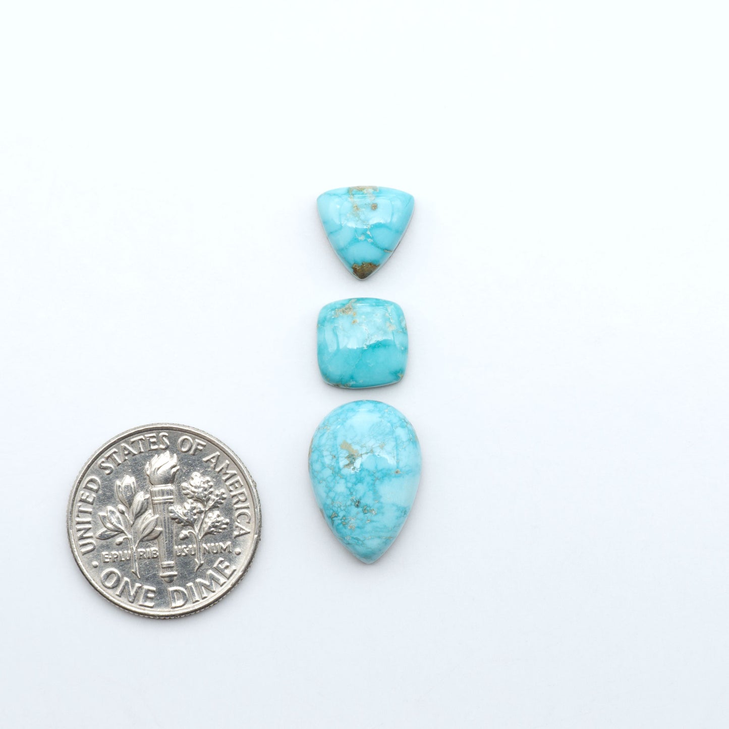 Fox Turquoise cabochons, polished gemstones with natural matrix on a white background, with a US dime for scale