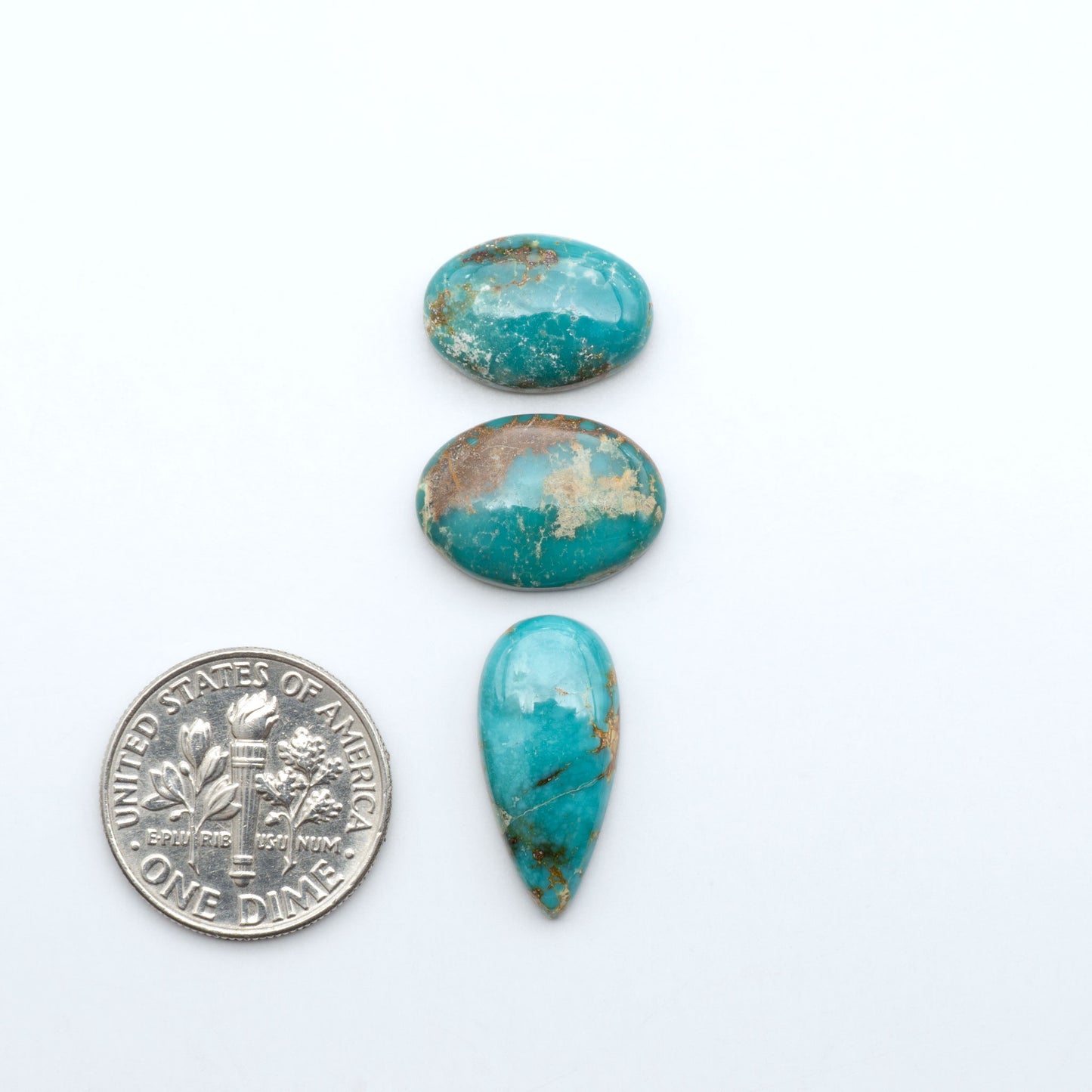 Fox Turquoise cabochons, polished gemstones with natural matrix on a white background, with a US dime for scale