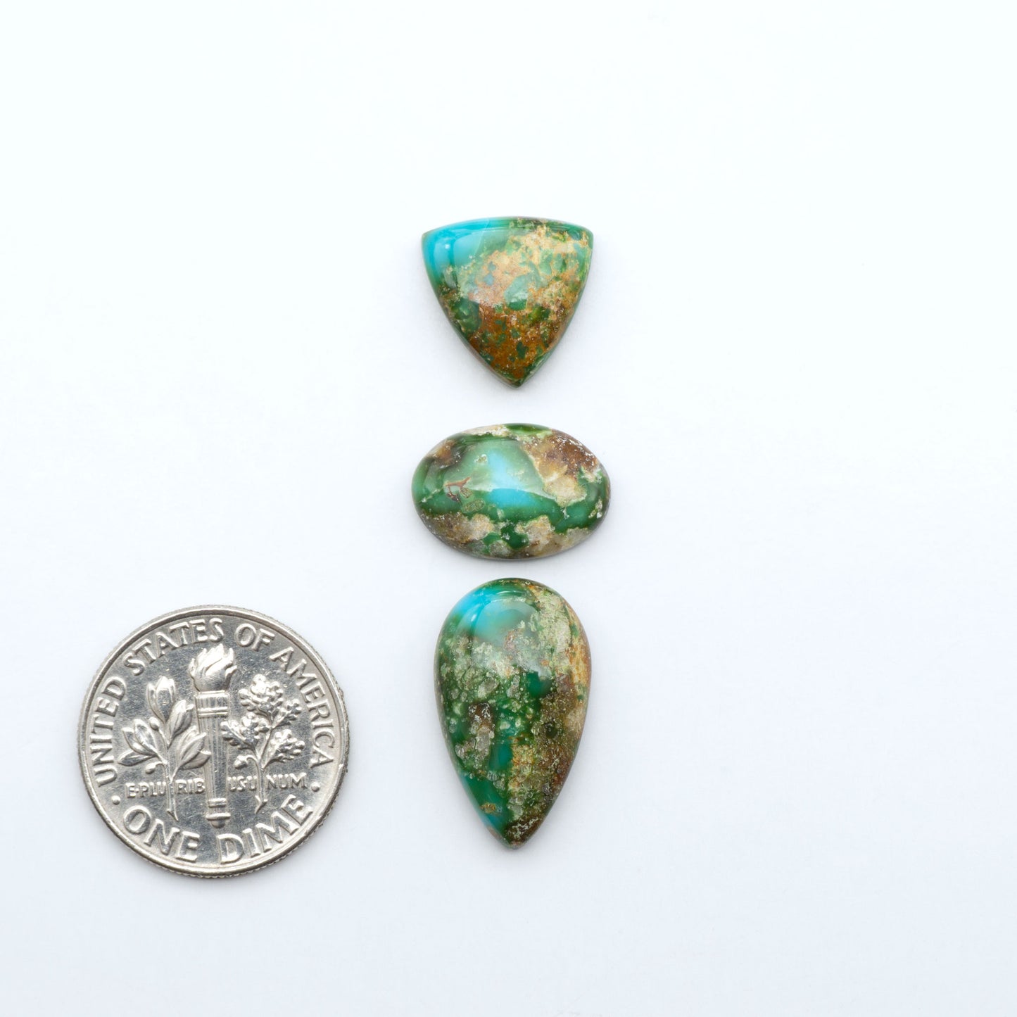 Sonoran Mountain Turquoise cabochons, blue-green color with natural matrix, polished stones on a white background, with a US dime for scale