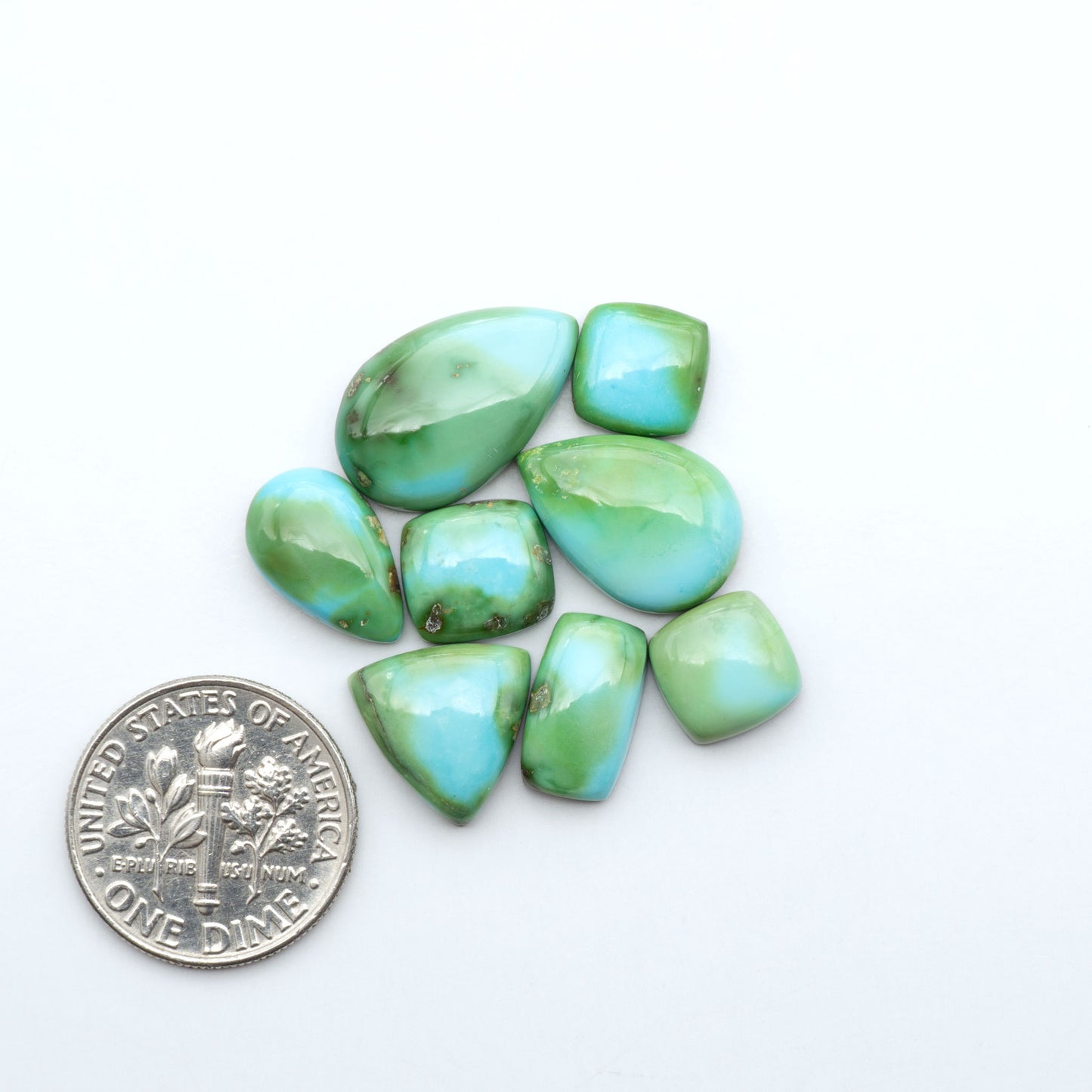 Sonoran Mountain Turquoise cabochons, blue-green color with natural matrix, polished stones on a white background, with a US dime for scale