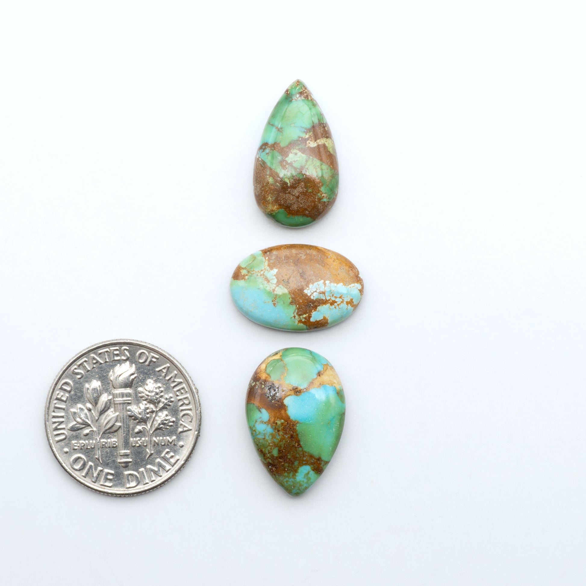 Sonoran Mountain Turquoise cabochons, blue-green color with natural matrix, polished stones on a white background, with a US dime for scale