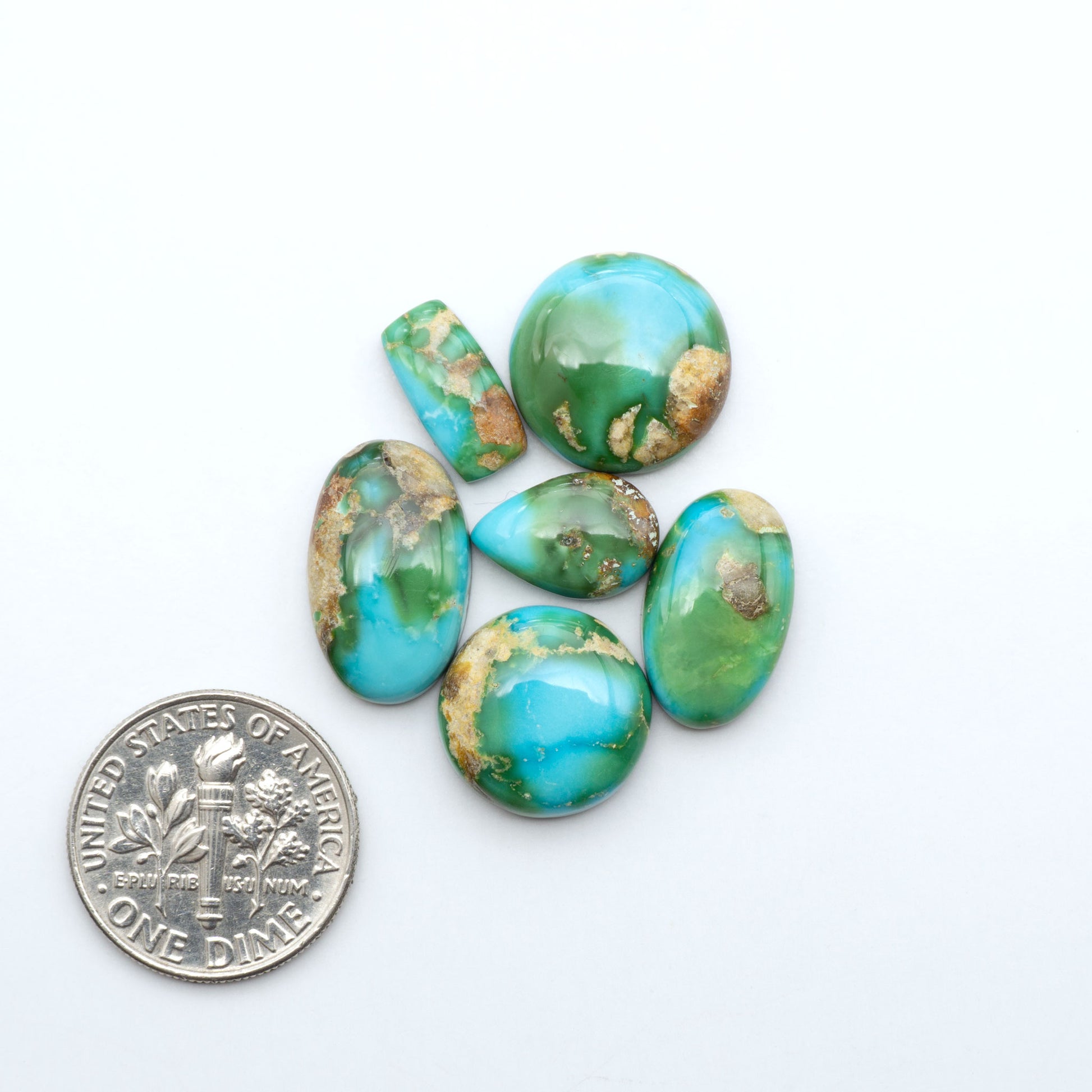 Sonoran Mountain Turquoise cabochons, blue-green color with natural matrix, polished stones on a white background, with a US dime for scale