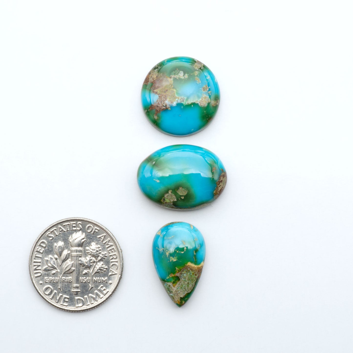 Sonoran Mountain Turquoise cabochons, blue-green color with natural matrix, polished stones on a white background, with a US dime for scale