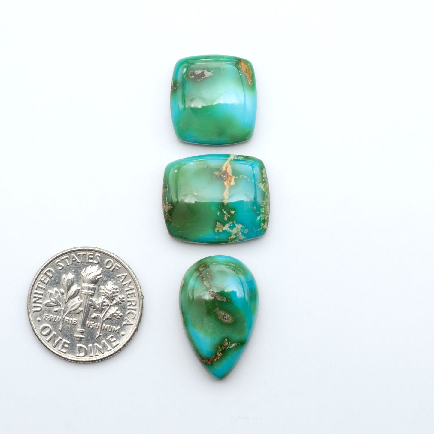 Sonoran Mountain Turquoise cabochons, blue-green color with natural matrix, polished stones on a white background, with a US dime for scale