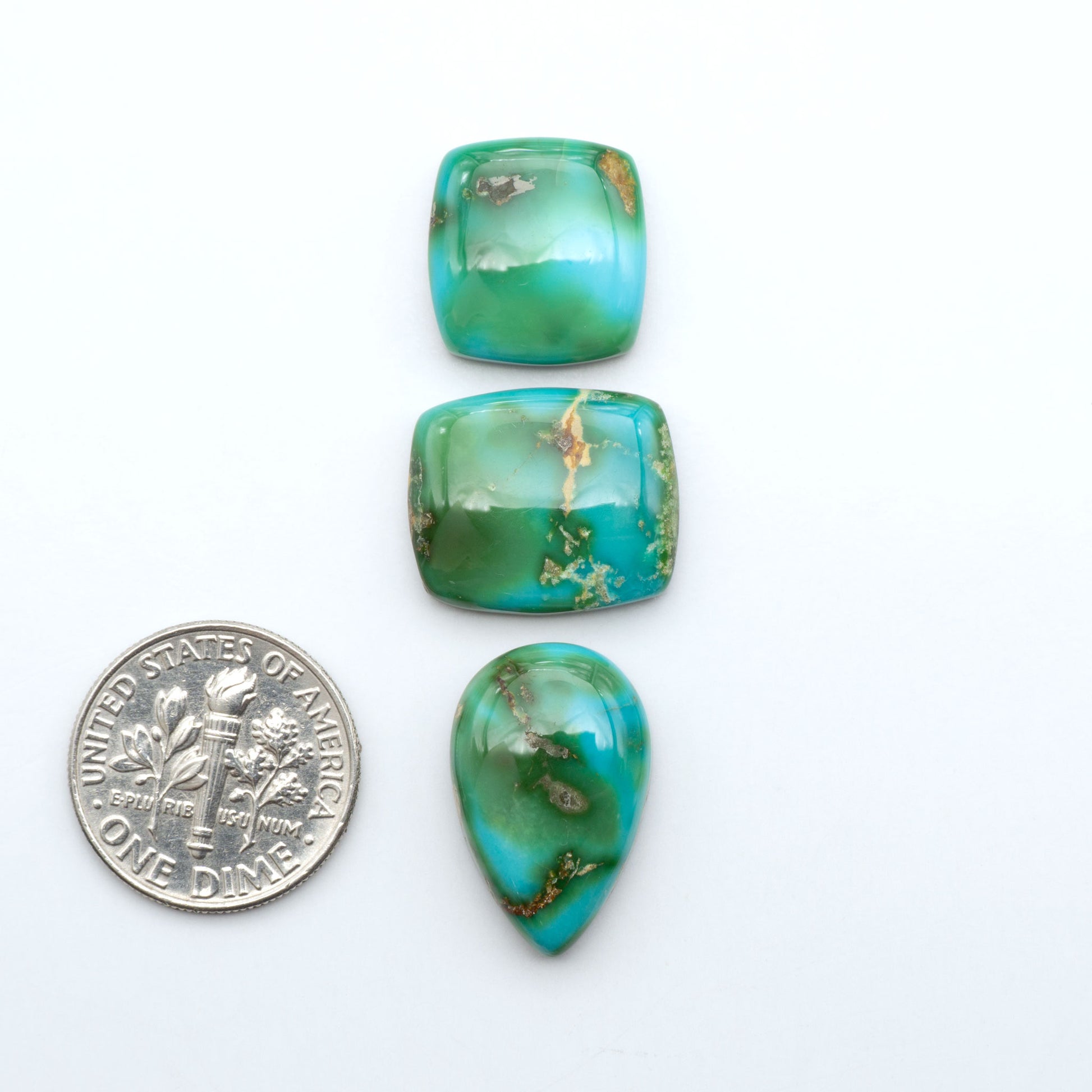 Sonoran Mountain Turquoise cabochons, blue-green color with natural matrix, polished stones on a white background, with a US dime for scale