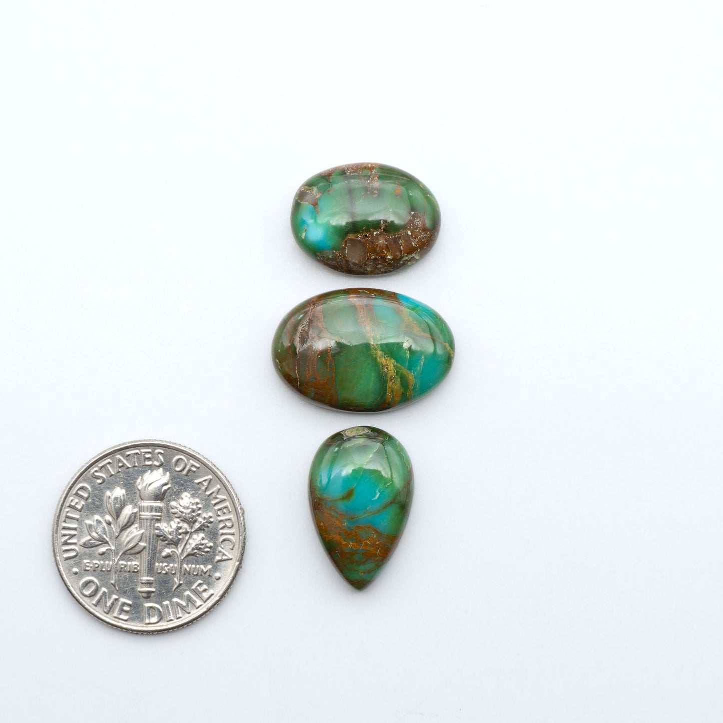 Sonoran Mountain Turquoise cabochons, blue-green color with natural matrix, polished stones on a white background, with a US dime for scale