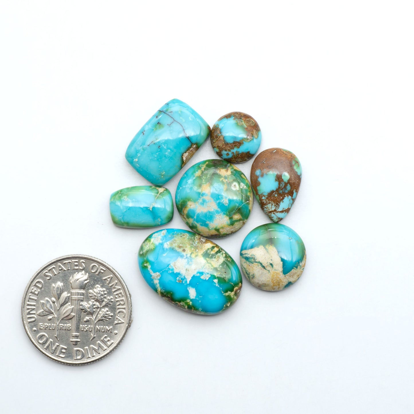 Sonoran Mountain Turquoise cabochons, blue-green color with natural matrix, polished stones on a white background, with a US dime for scale