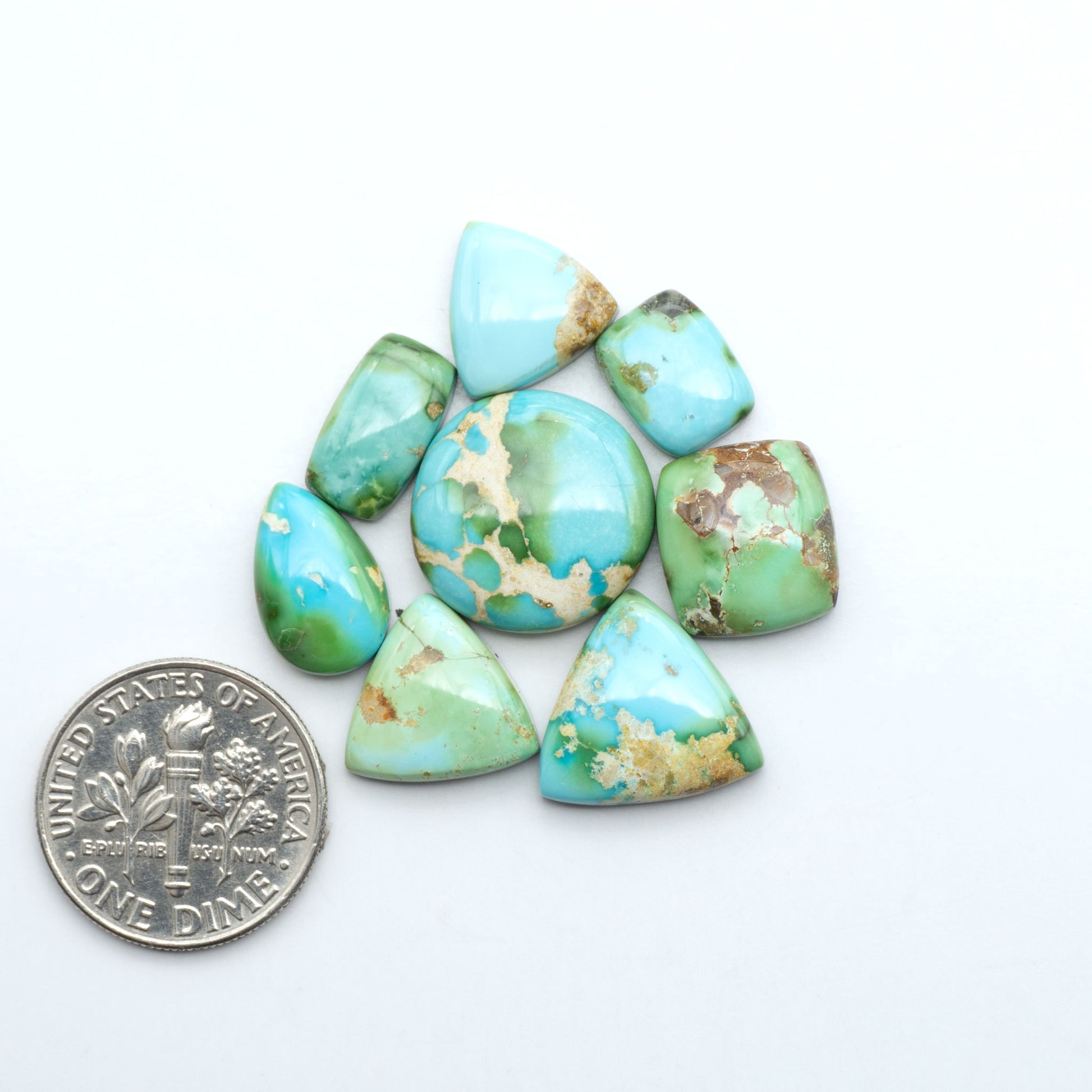 Sonoran Mountain Turquoise cabochons, blue-green color with natural matrix, polished stones on a white background, with a US dime for scale