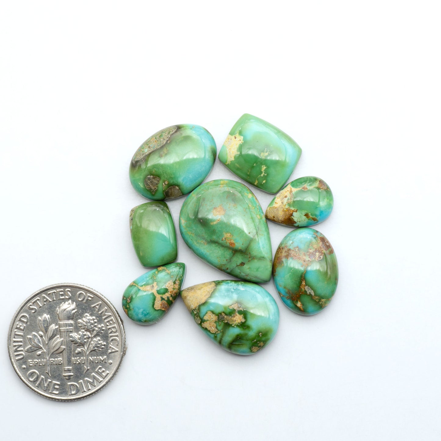 Sonoran Mountain Turquoise cabochons, blue-green color with natural matrix, polished stones on a white background, with a US dime for scale