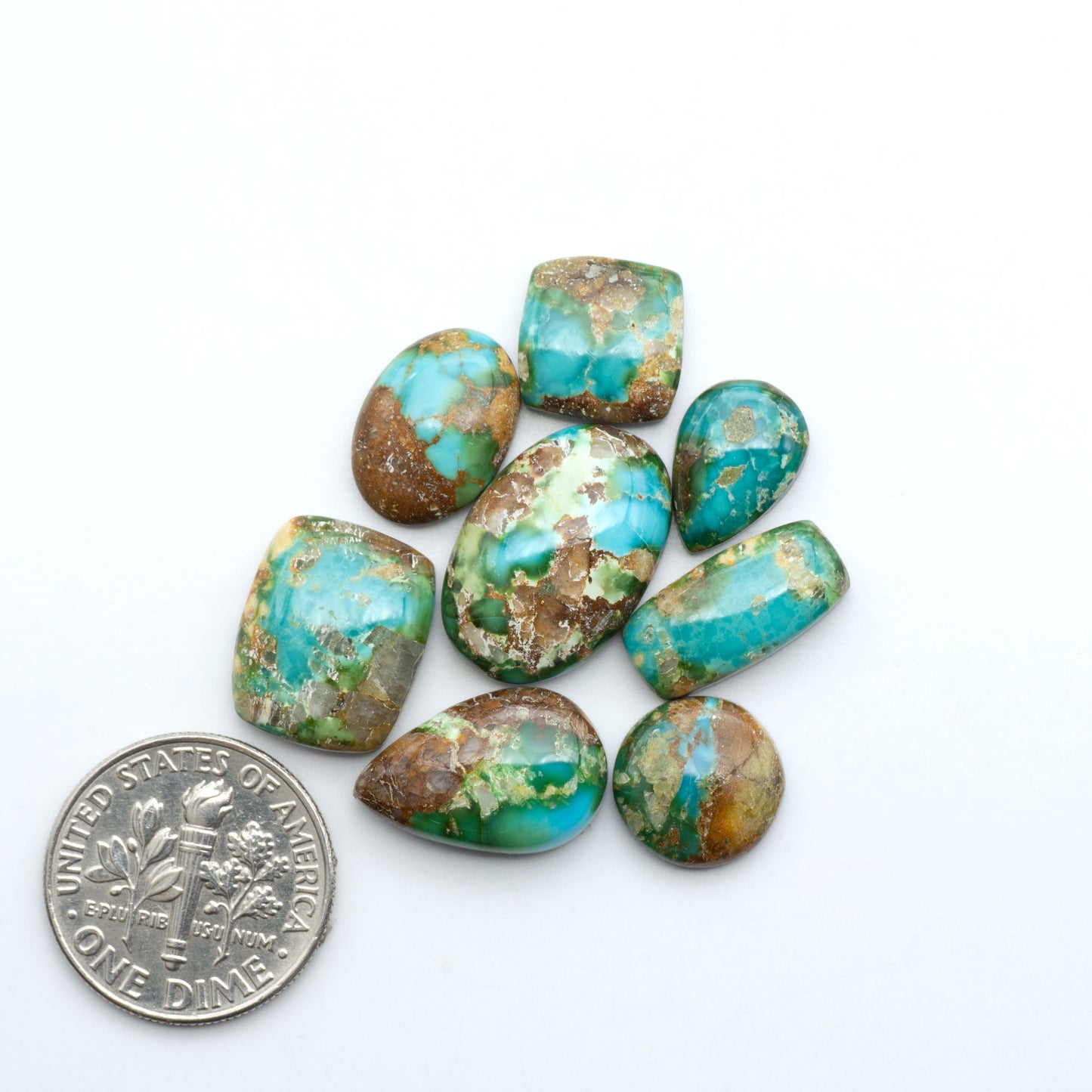Sonoran Mountain Turquoise cabochons, blue-green color with natural matrix, polished stones on a white background, with a US dime for scale