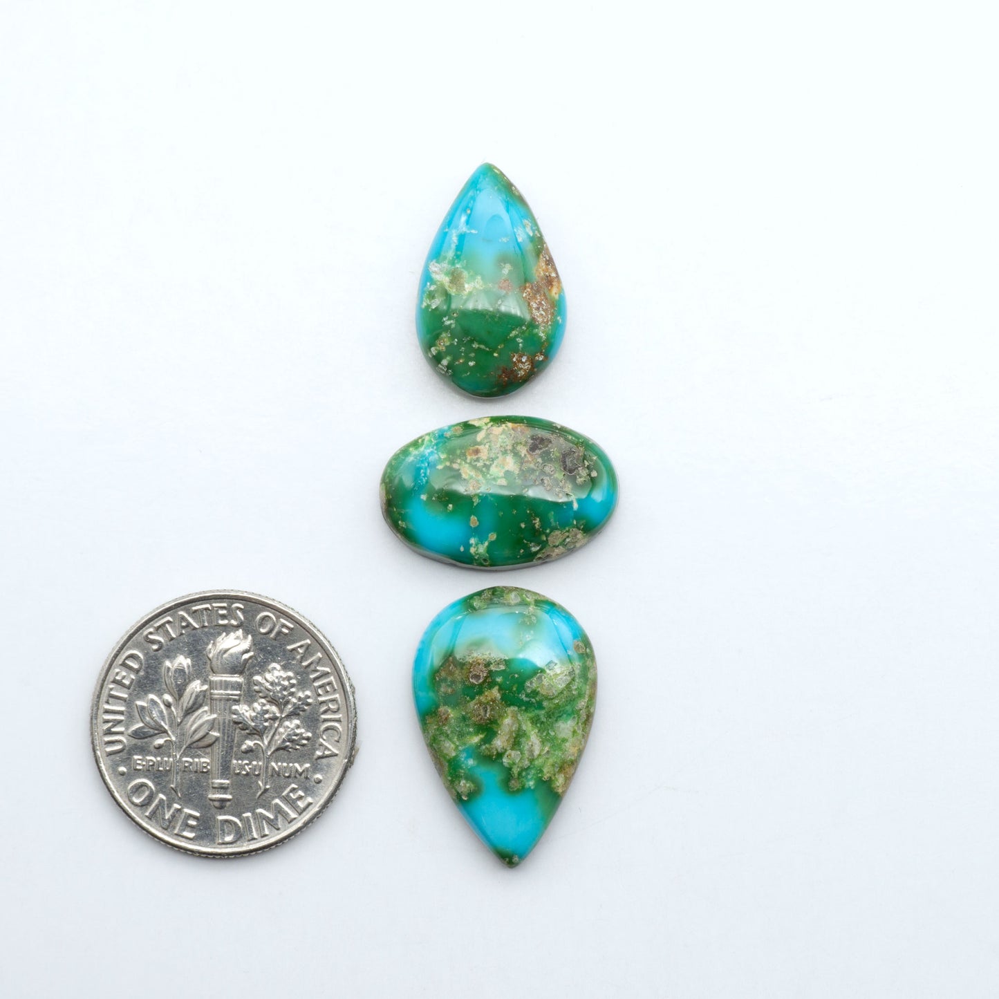 Sonoran Mountain Turquoise cabochons, blue-green color with natural matrix, polished stones on a white background, with a US dime for scale
