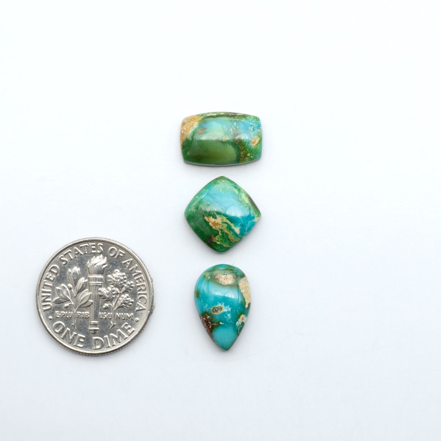 Sonoran Mountain Turquoise cabochons, blue-green color with natural matrix, polished stones on a white background, with a US dime for scale