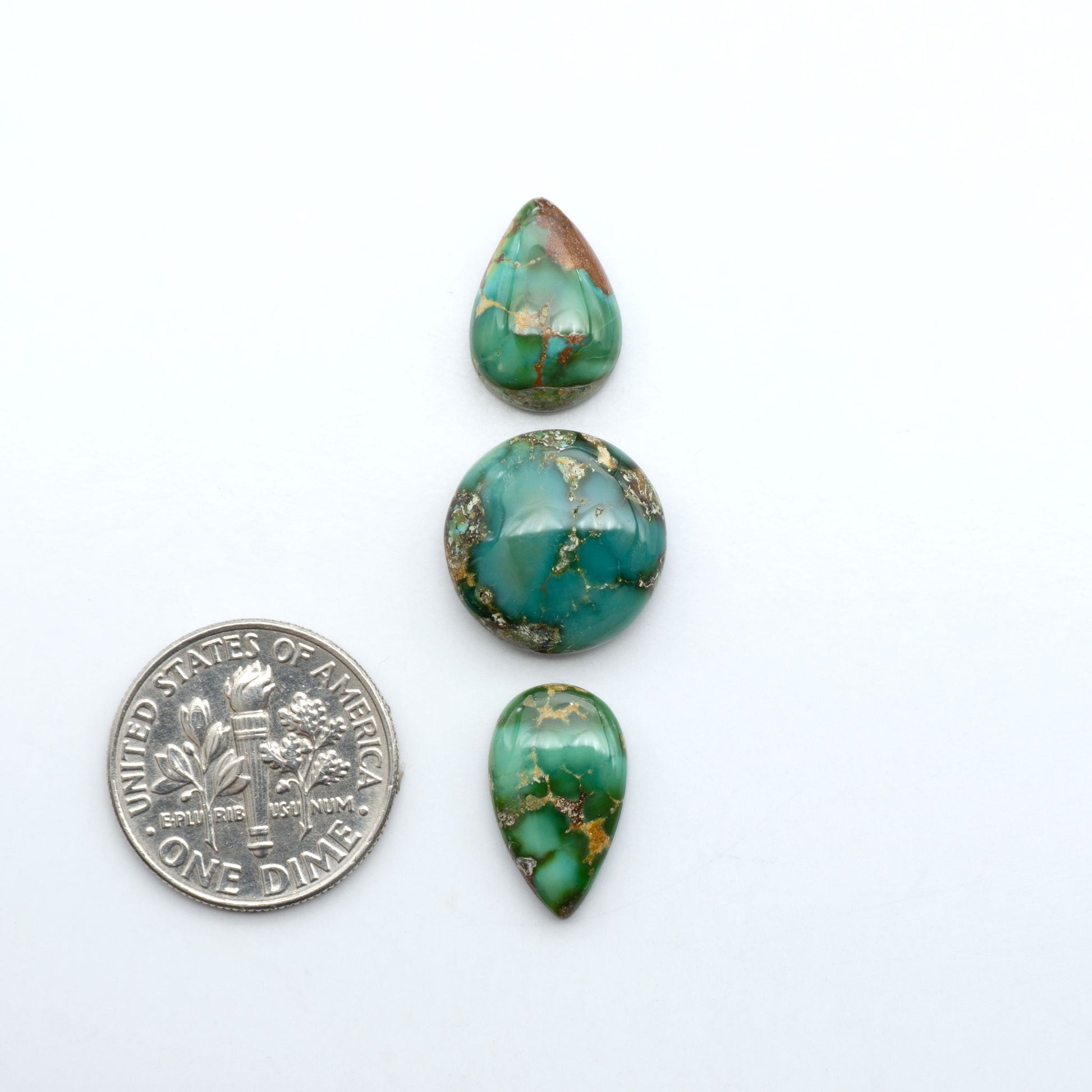 Sonoran Mountain Turquoise cabochons, blue-green color with natural matrix, polished stones on a white background, with a US dime for scale