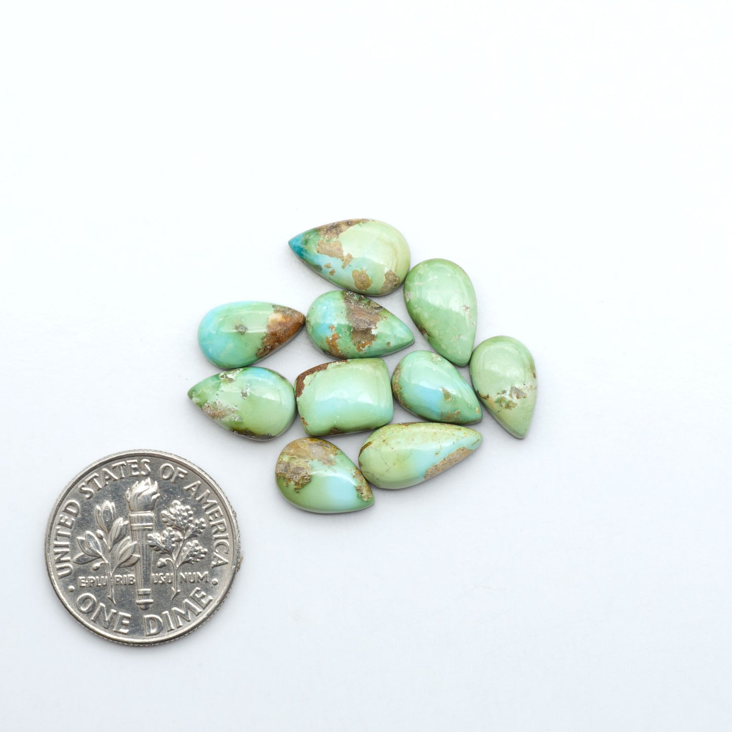 Sonoran Mountain Turquoise cabochons, blue-green color with natural matrix, polished stones on a white background, with a US dime for scale