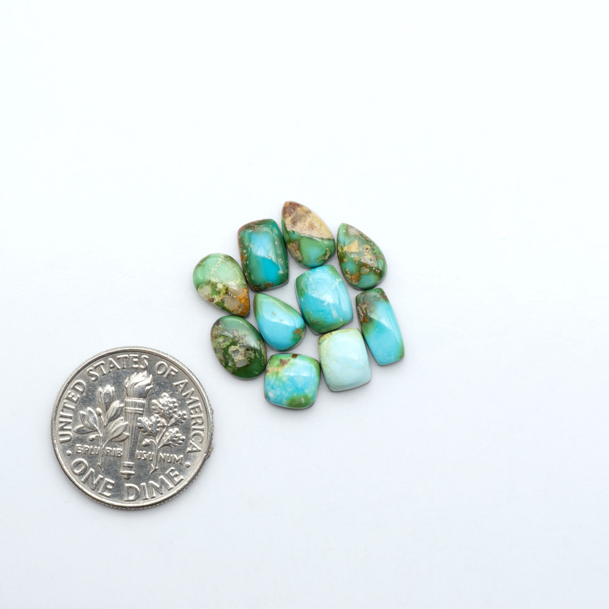 Sonoran Mountain Turquoise cabochons, blue-green color with natural matrix, polished stones on a white background, with a US dime for scale