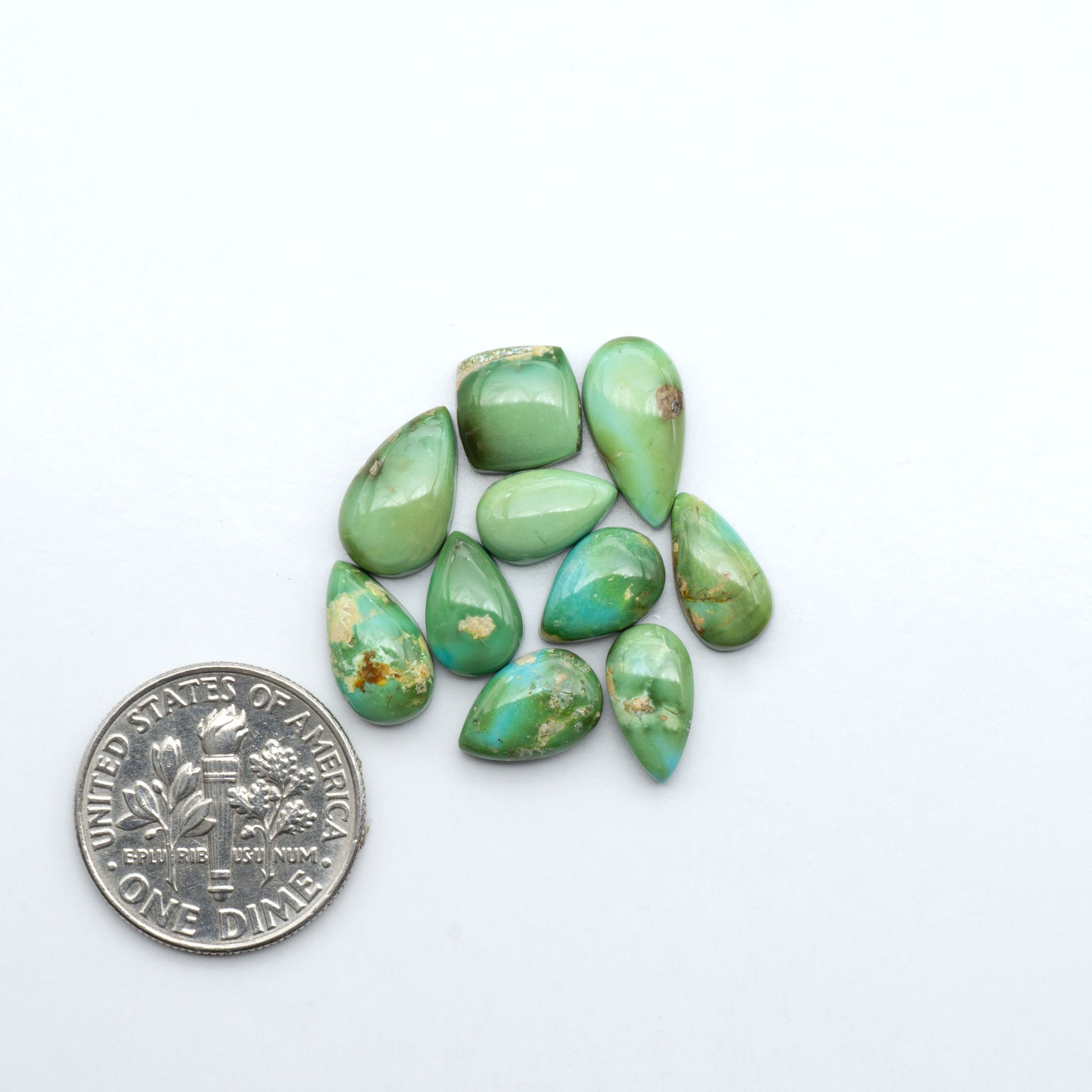 Sonoran Mountain Turquoise cabochons, blue-green color with natural matrix, polished stones on a white background, with a US dime for scale