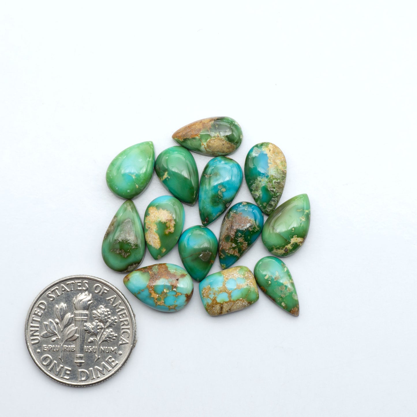 Sonoran Mountain Turquoise cabochons, blue-green color with natural matrix, polished stones on a white background, with a US dime for scale
