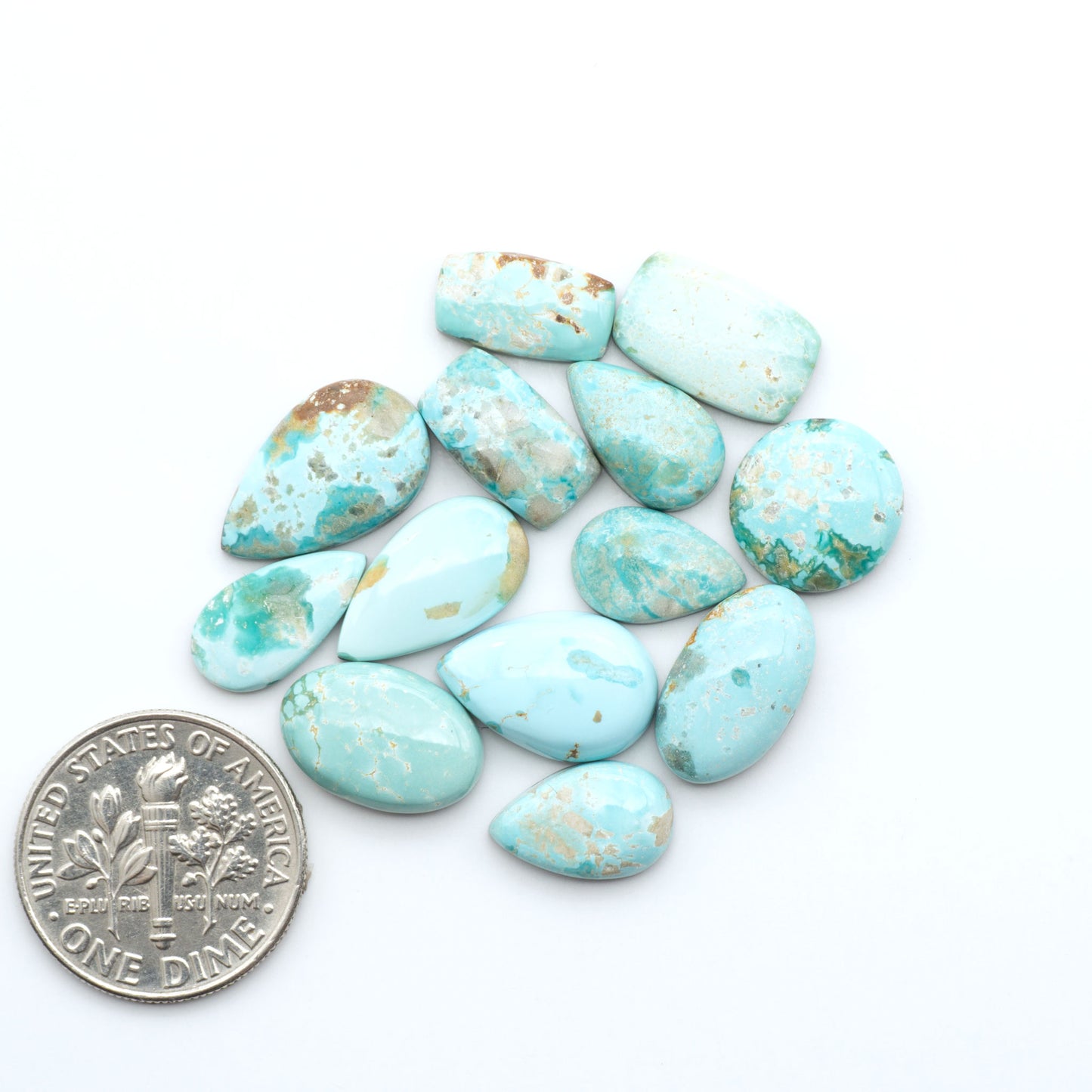 Fox Turquoise cabochons, polished gemstones with natural matrix on a white background, with a US dime for scale