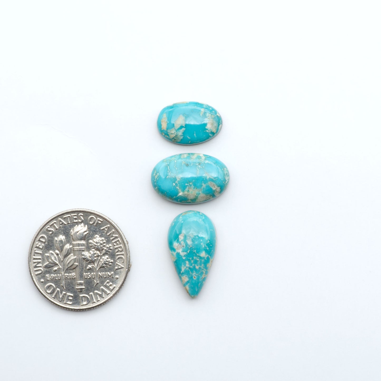 Fox Turquoise cabochons, polished gemstones with natural matrix on a white background, with a US dime for scale