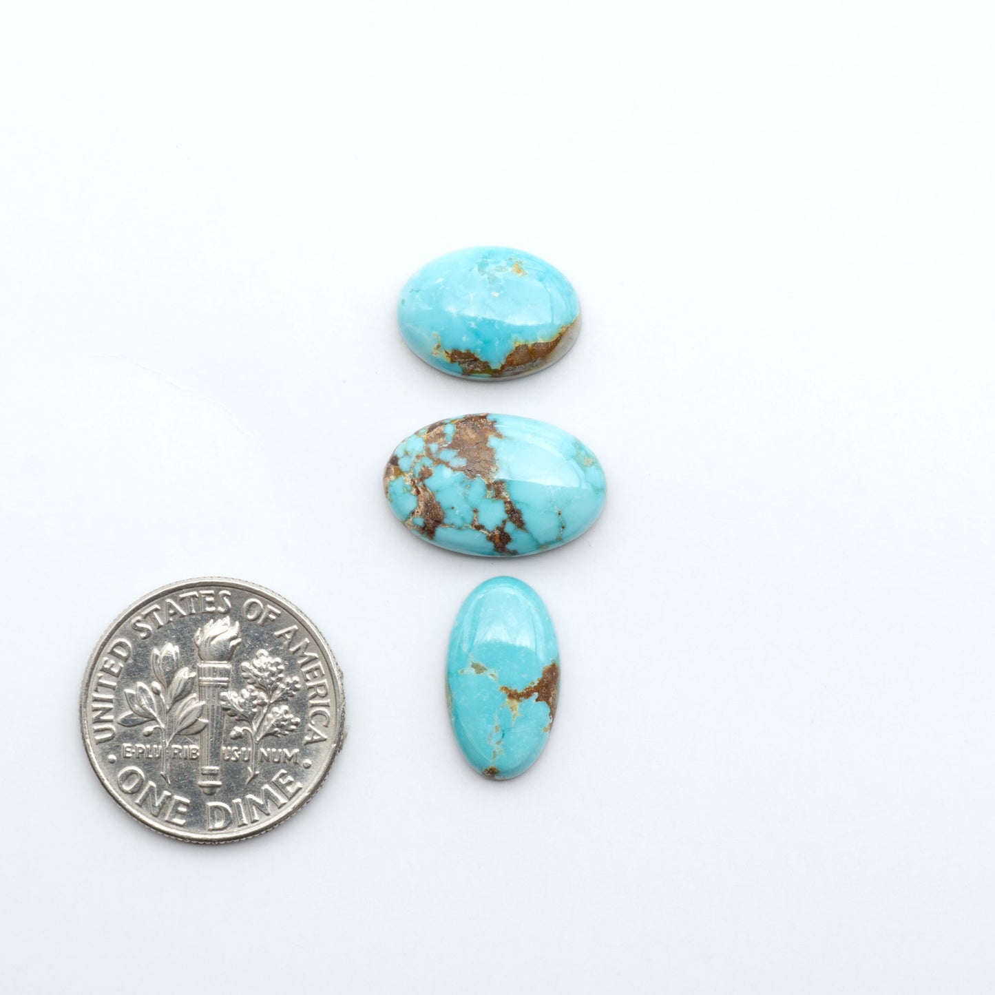 Fox Turquoise cabochons, polished gemstones with natural matrix on a white background, with a US dime for scale