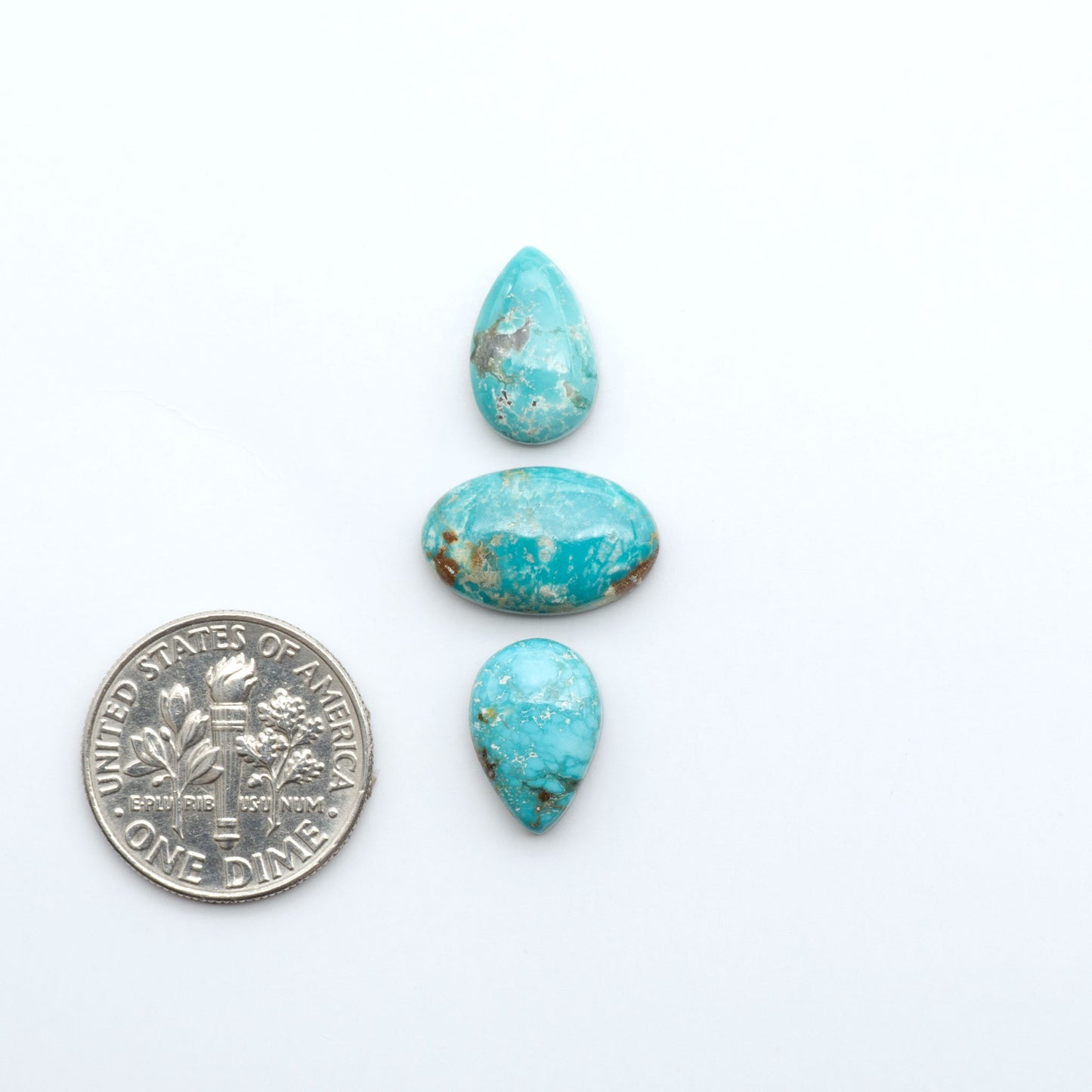 Fox Turquoise cabochons, polished gemstones with natural matrix on a white background, with a US dime for scale